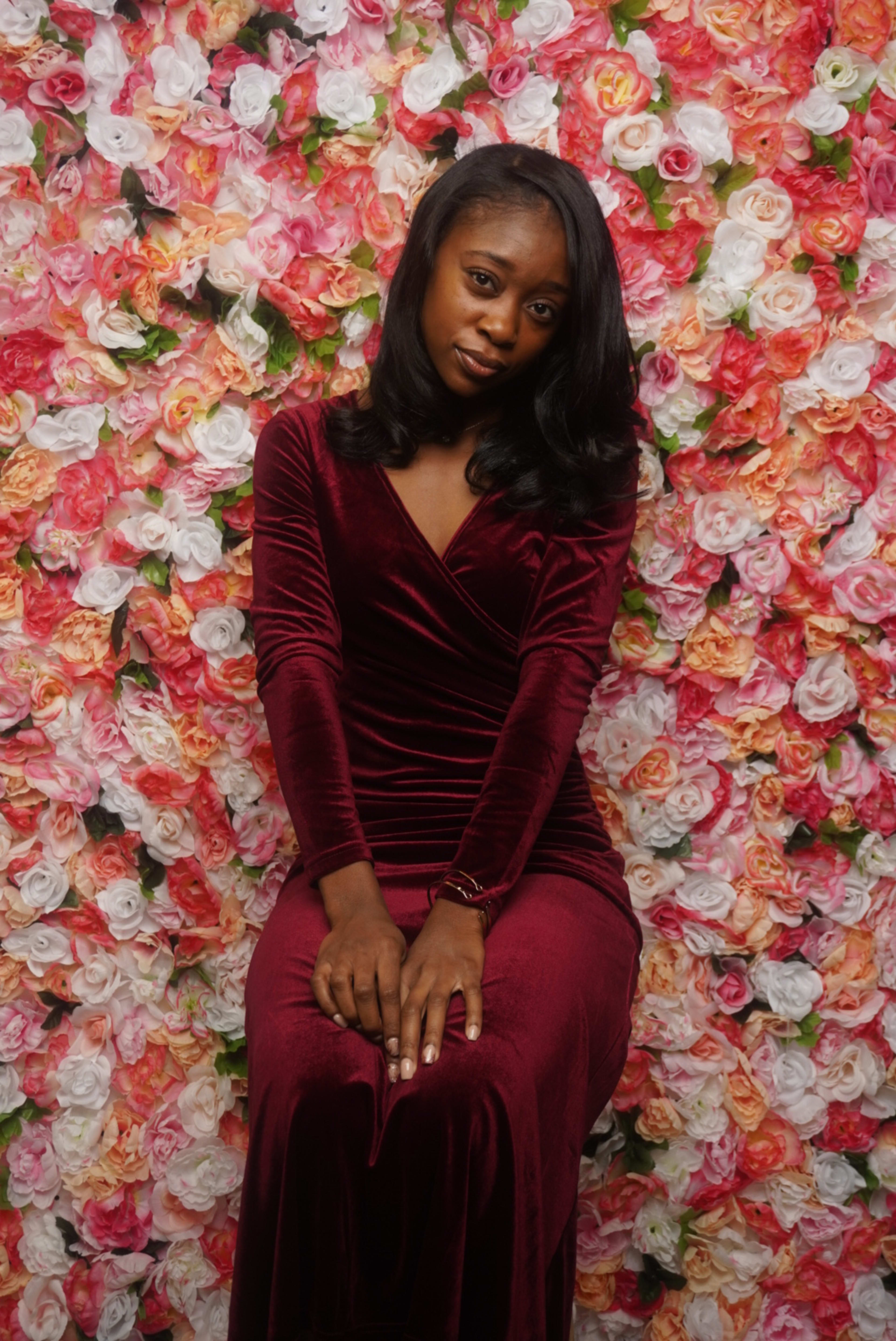 A woman in a red dress posing for a garden photoshoot on a bed of flowers.