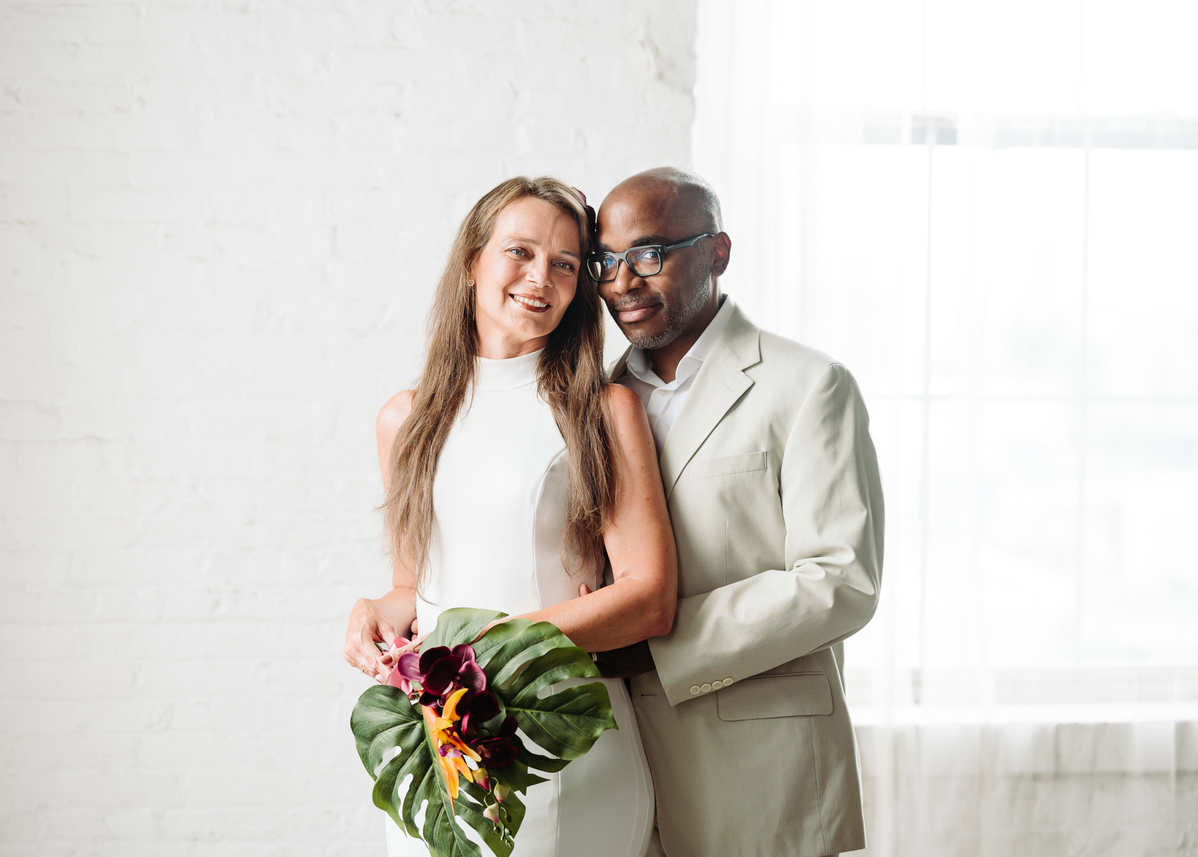 Un couple posant au cours d'un shooting photo minimaliste en blanc et beige et tenant des plantes.