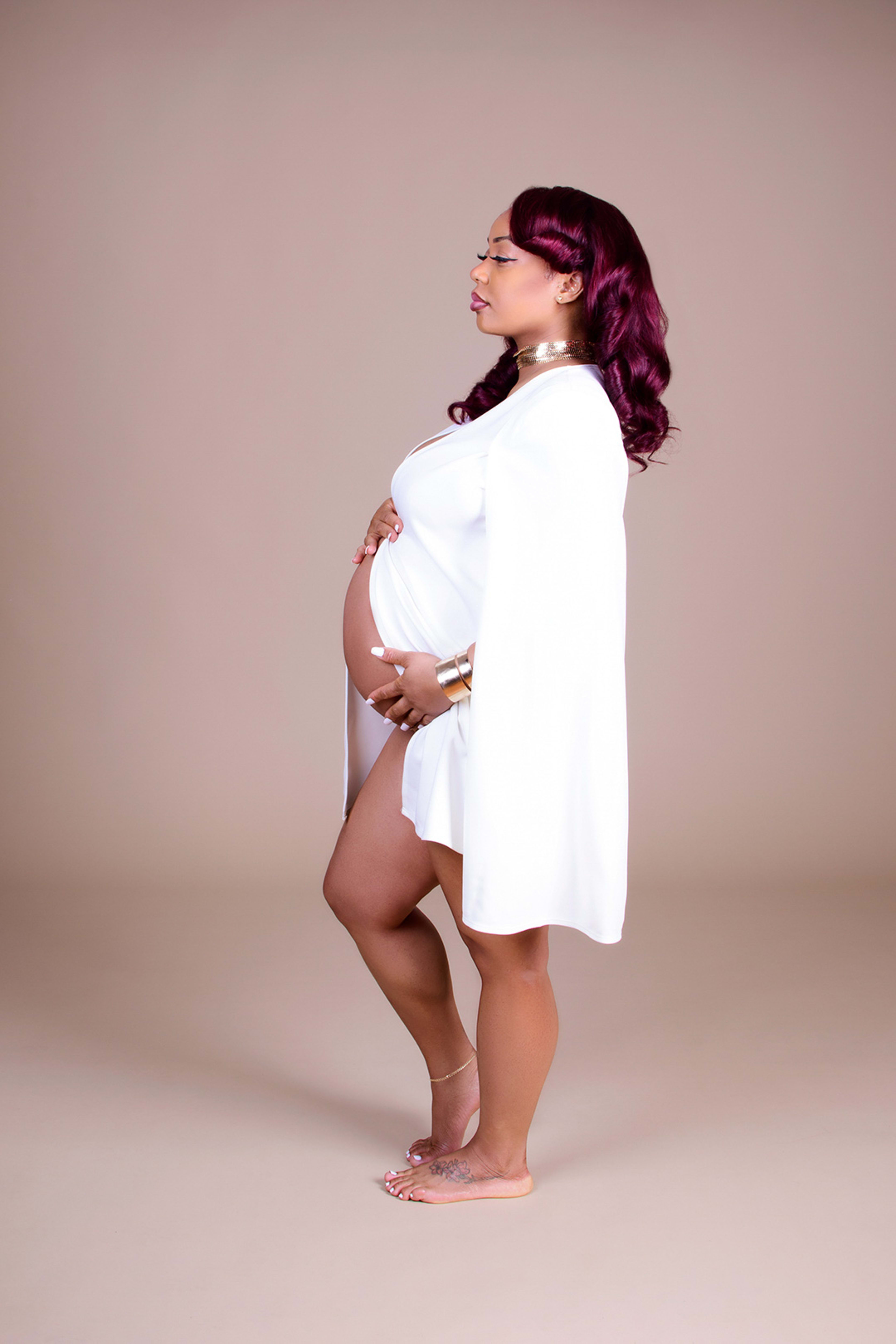 A maternity photoshoot with a pregnant woman wearing a white dress.