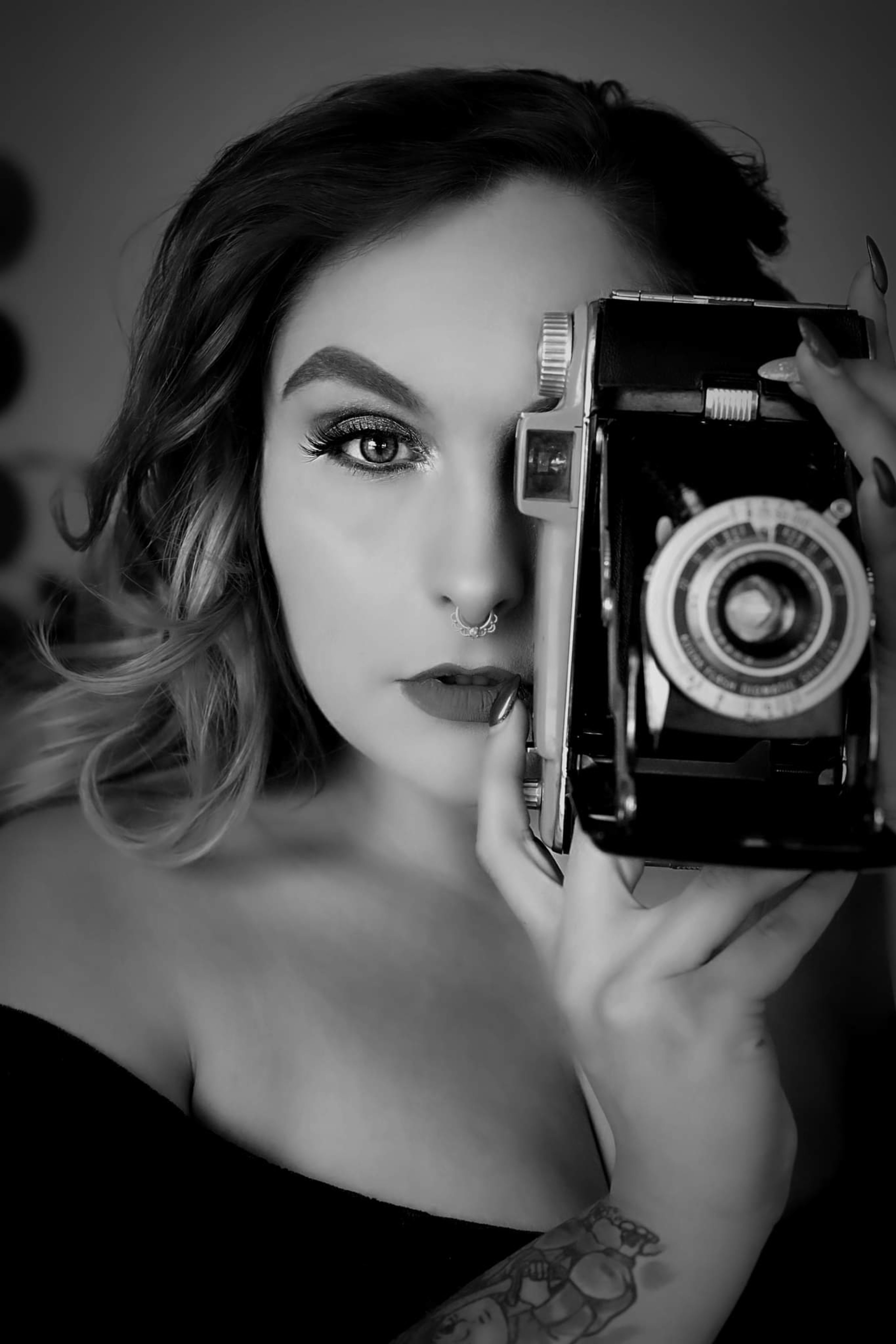 A black and white photoshoot of a woman holding a retro camera up to her face.