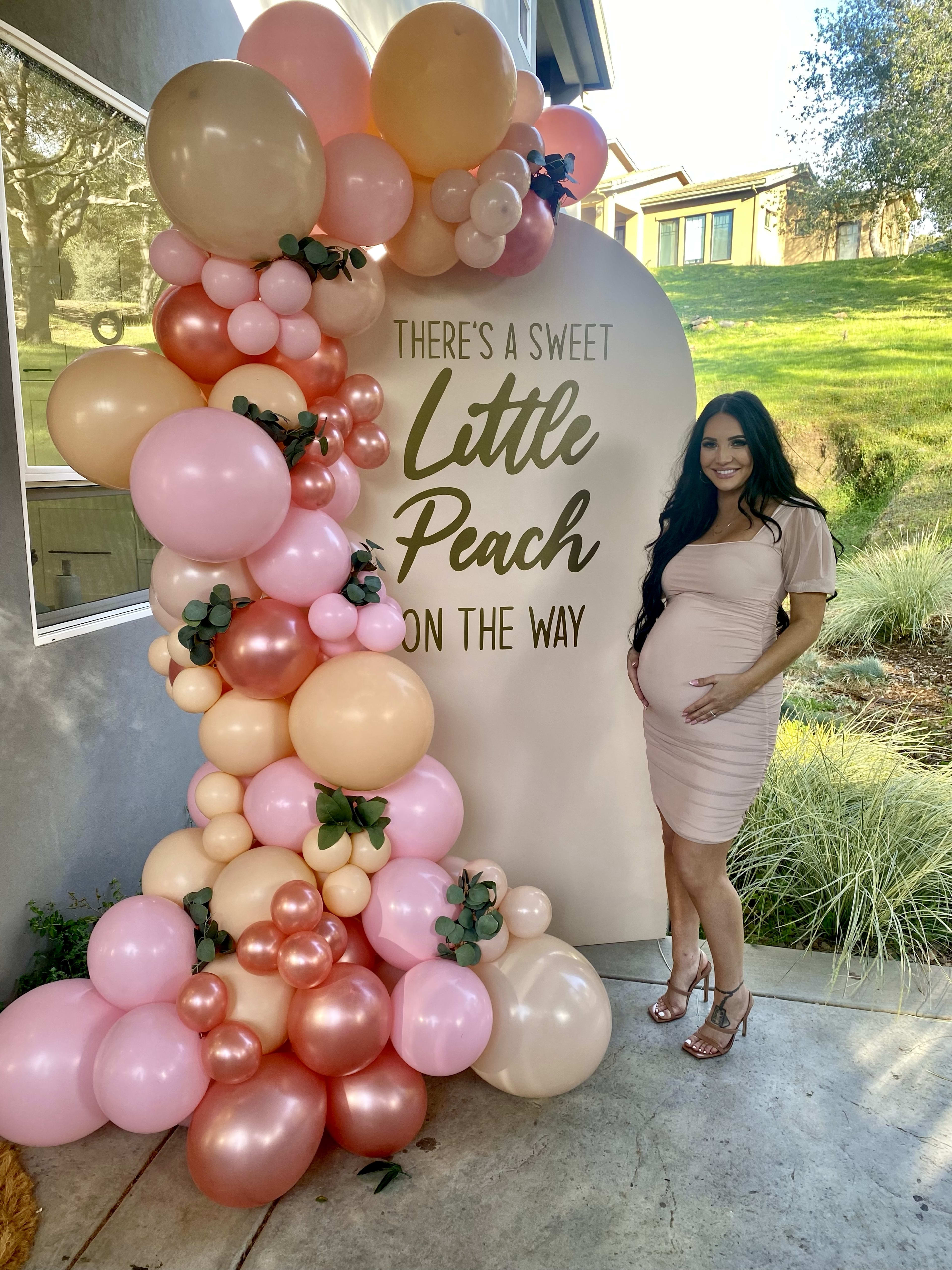 Eine schwangere Frau, die vor einem Babyparty-Schild mit rosafarbenen Ballons steht.