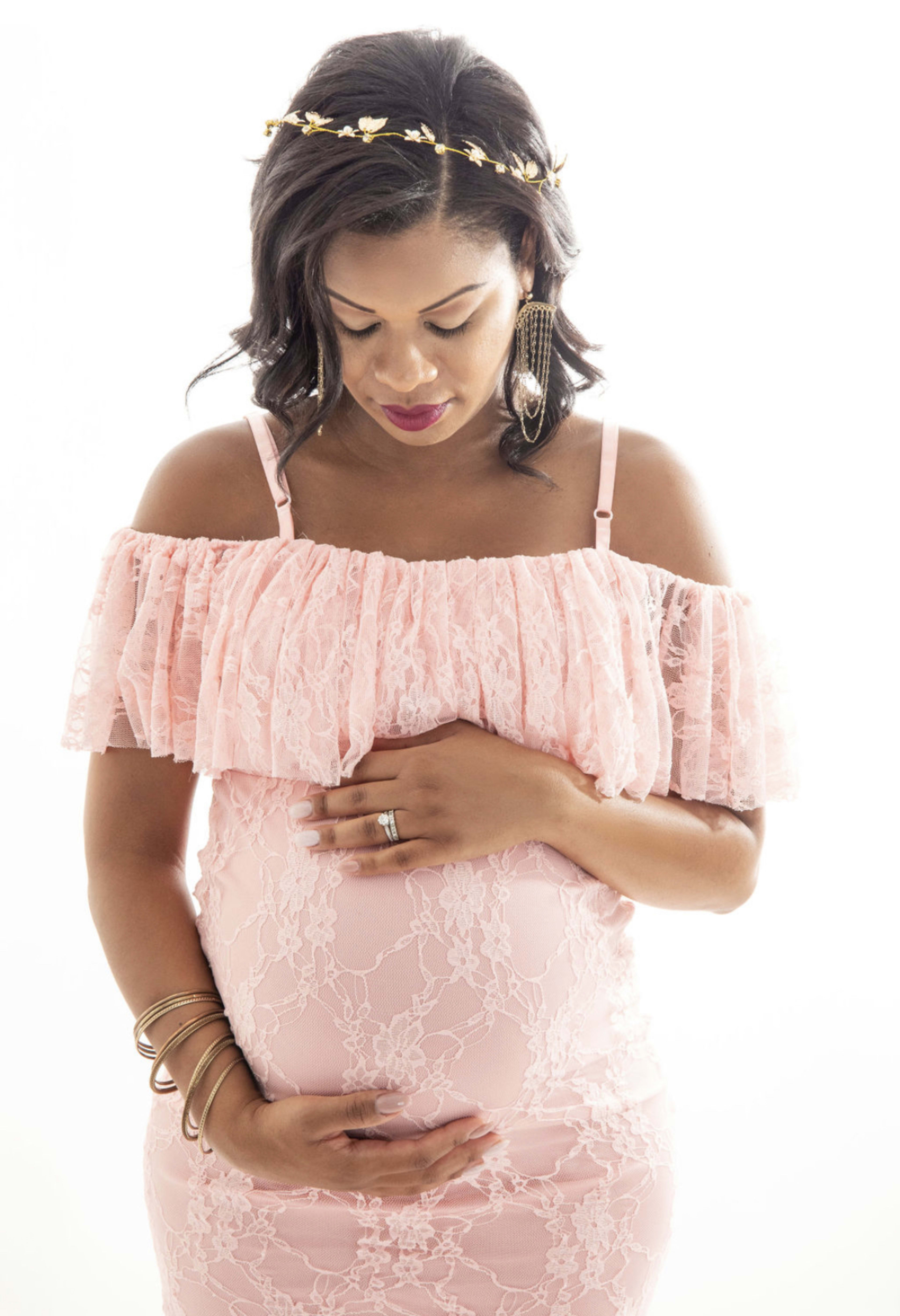 Eine schwangere Frau in einem rosafarbenen Boho-Kleid, die für ein Schwangerschaftsfoto ihren Bauch umschlingt.