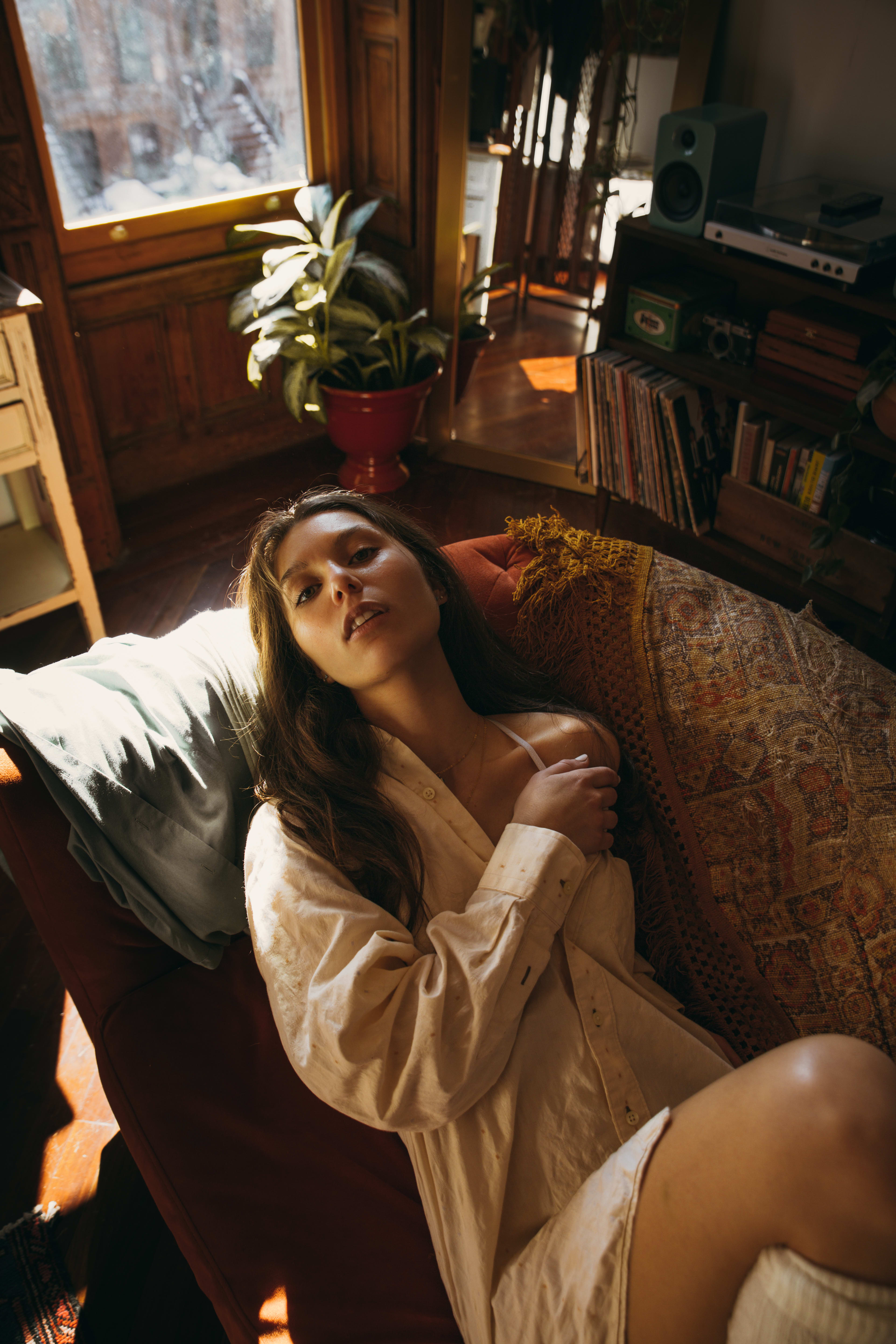 A boudoir photo shoot of a woman on a beige ledge near a window, wearing lingerie.