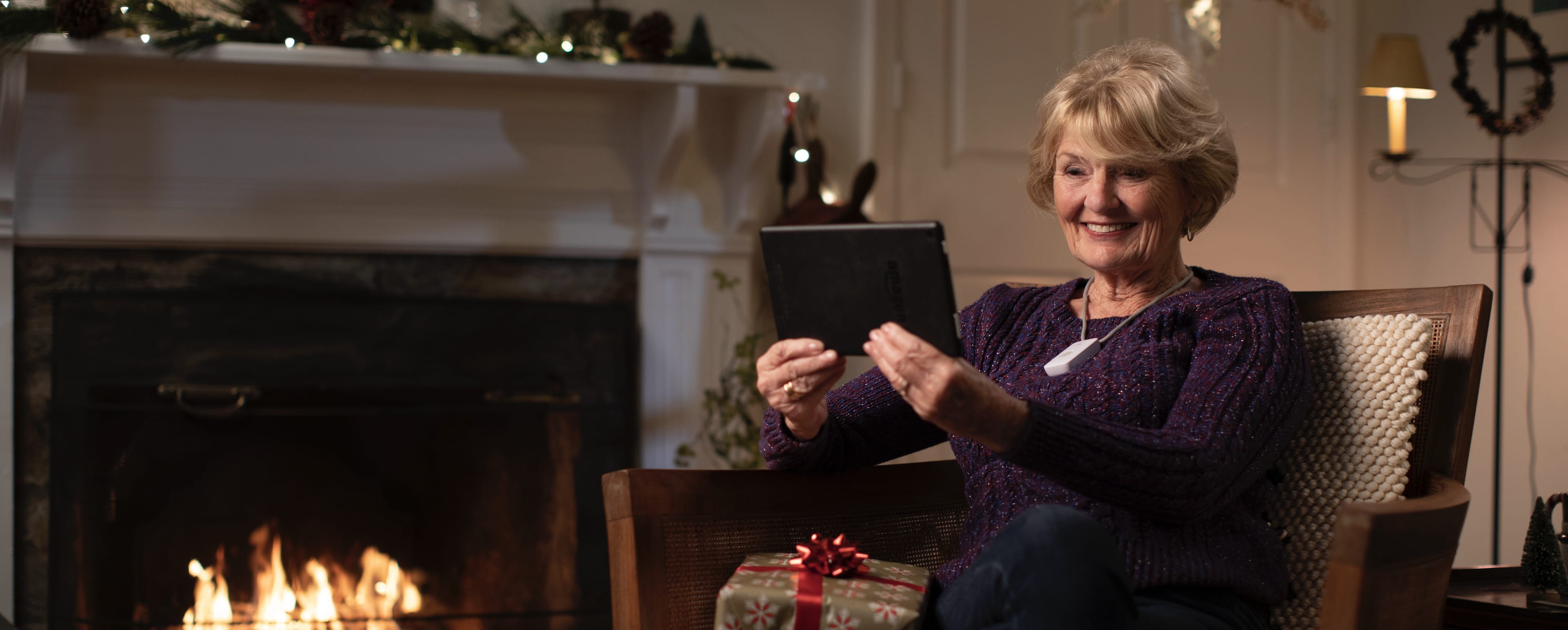 A woman posing for a winter photoshoot holding a tablet in front of a fireplace.