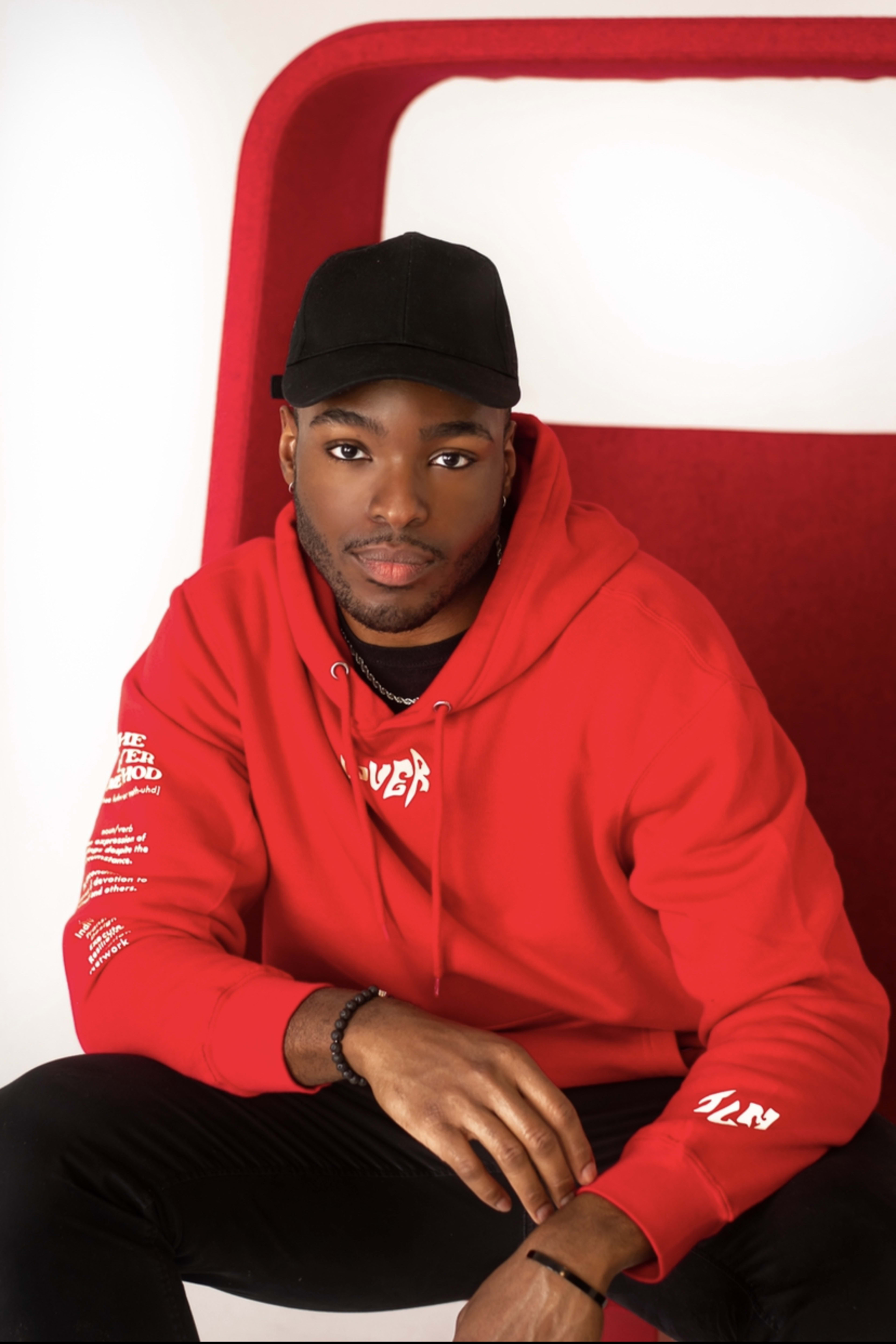 A man in a red hoodie posing for a photoshoot on a red chair.