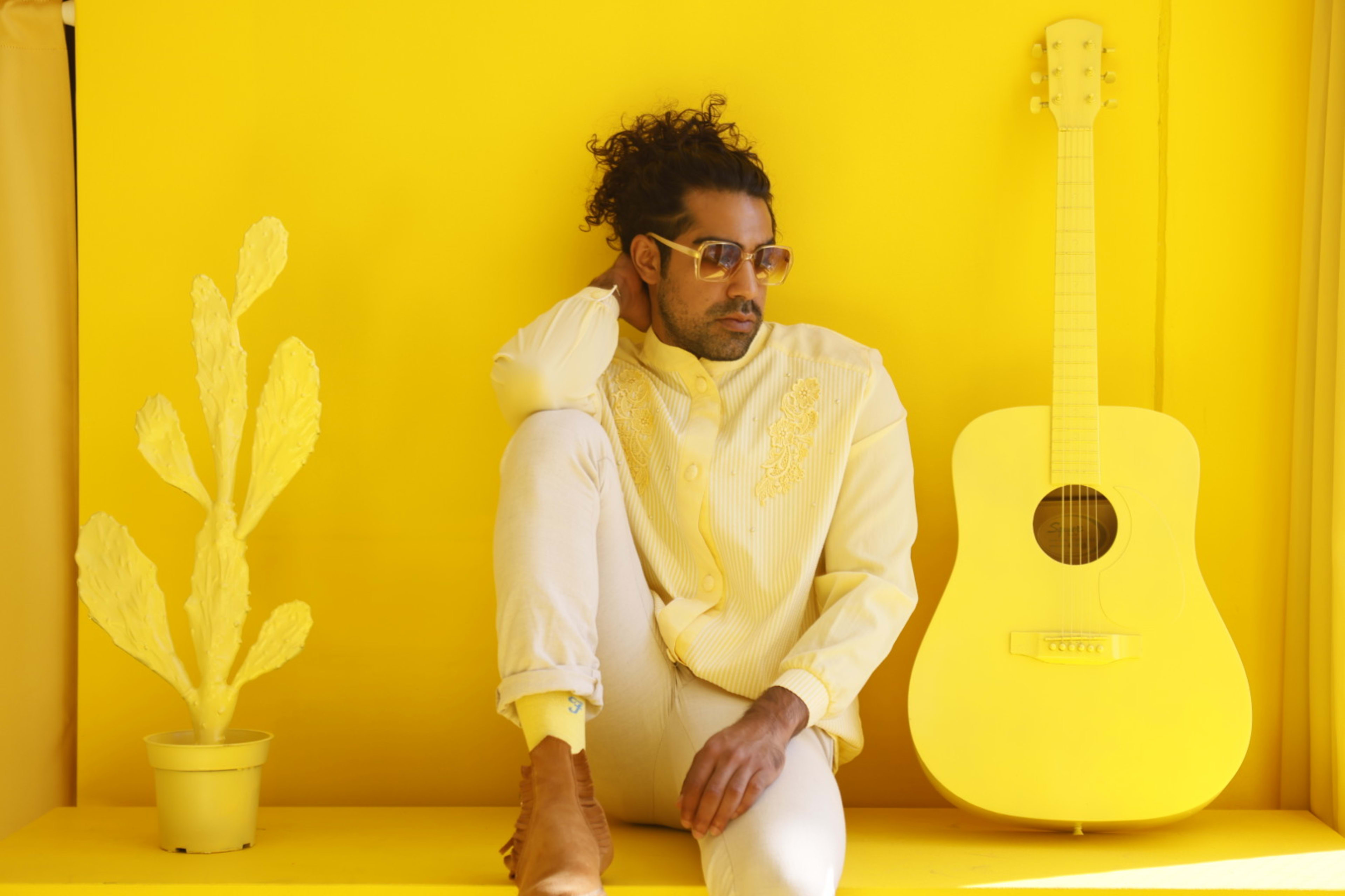 A retro photoshoot featuring a man sitting on a yellow shelf with a guitar.
