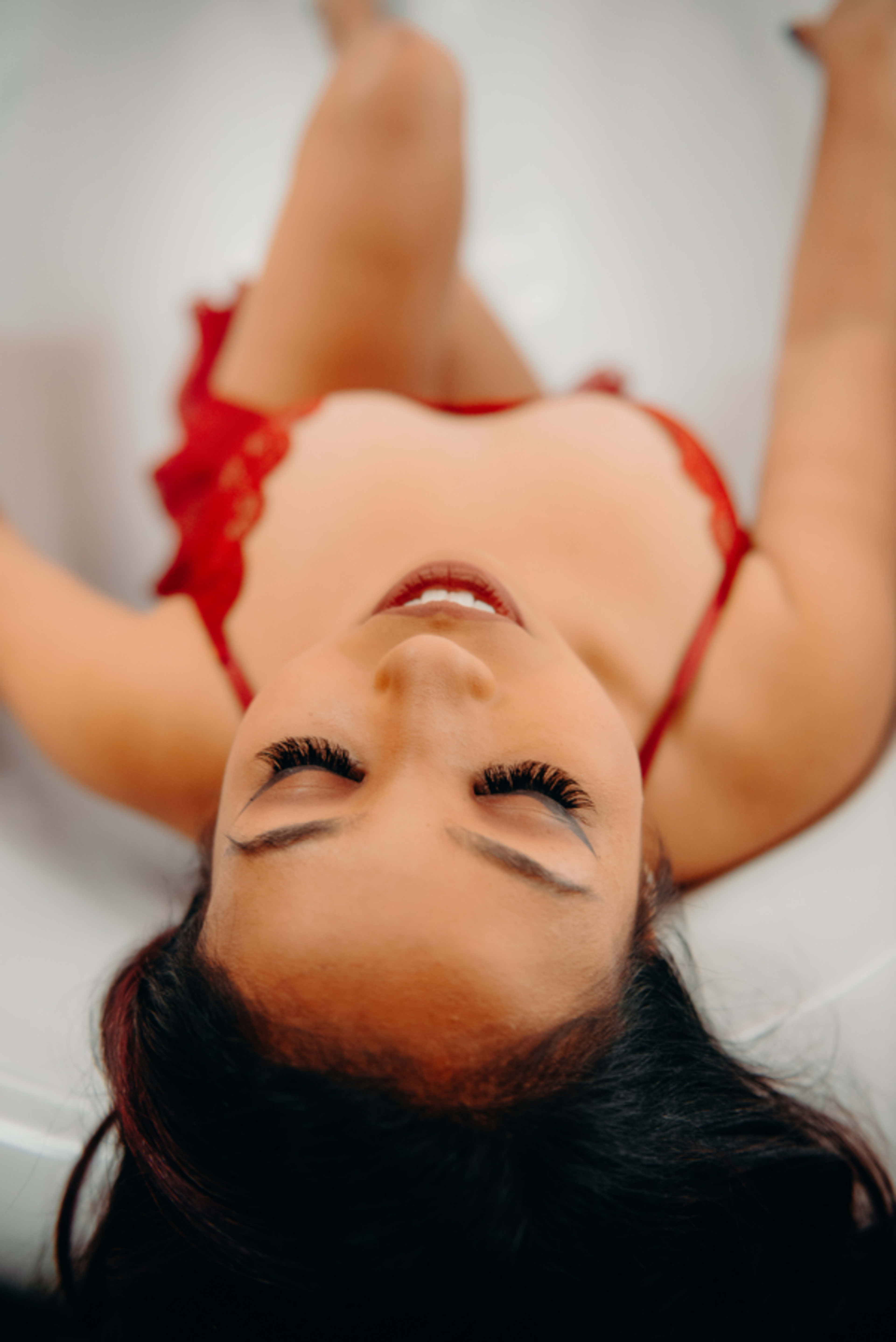 A red bikini-clad woman poses for a boudoir photo shoot in a white bath.