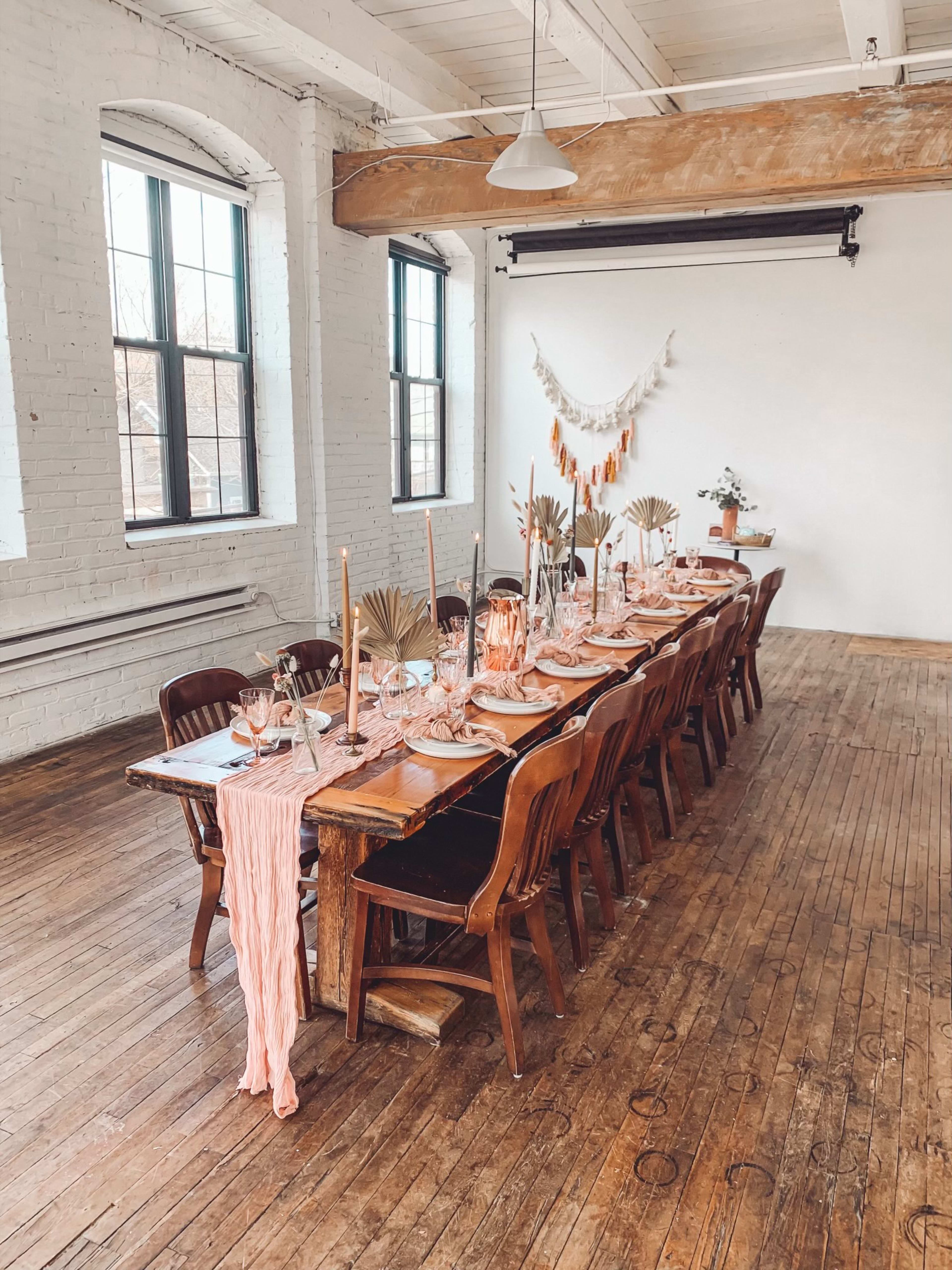 Une longue table rustique est dressée dans une grande salle pour un brunch de baby shower neutre.