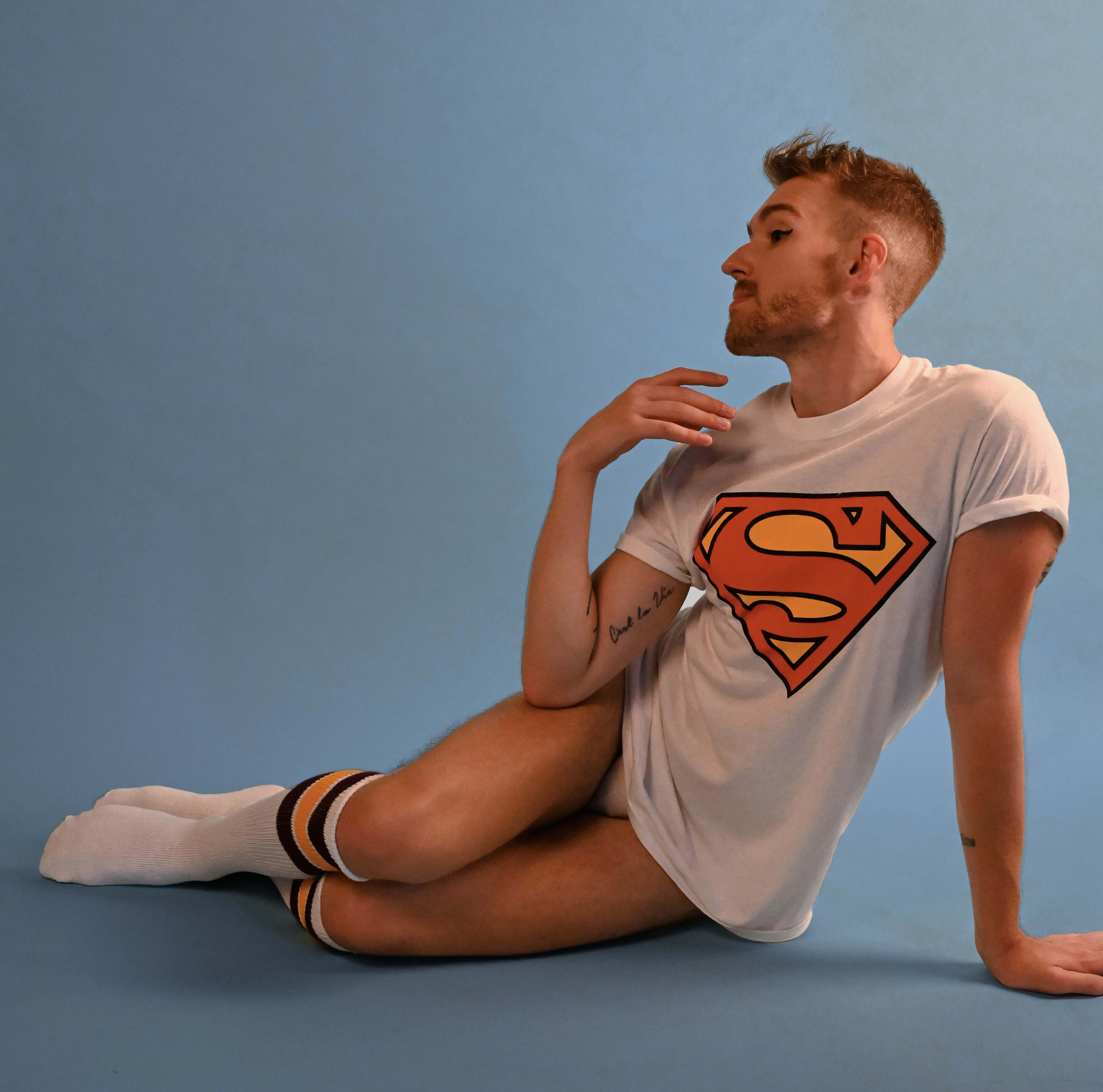 A man with a Superman t-shirt sitting on the ground for a photoshoot.