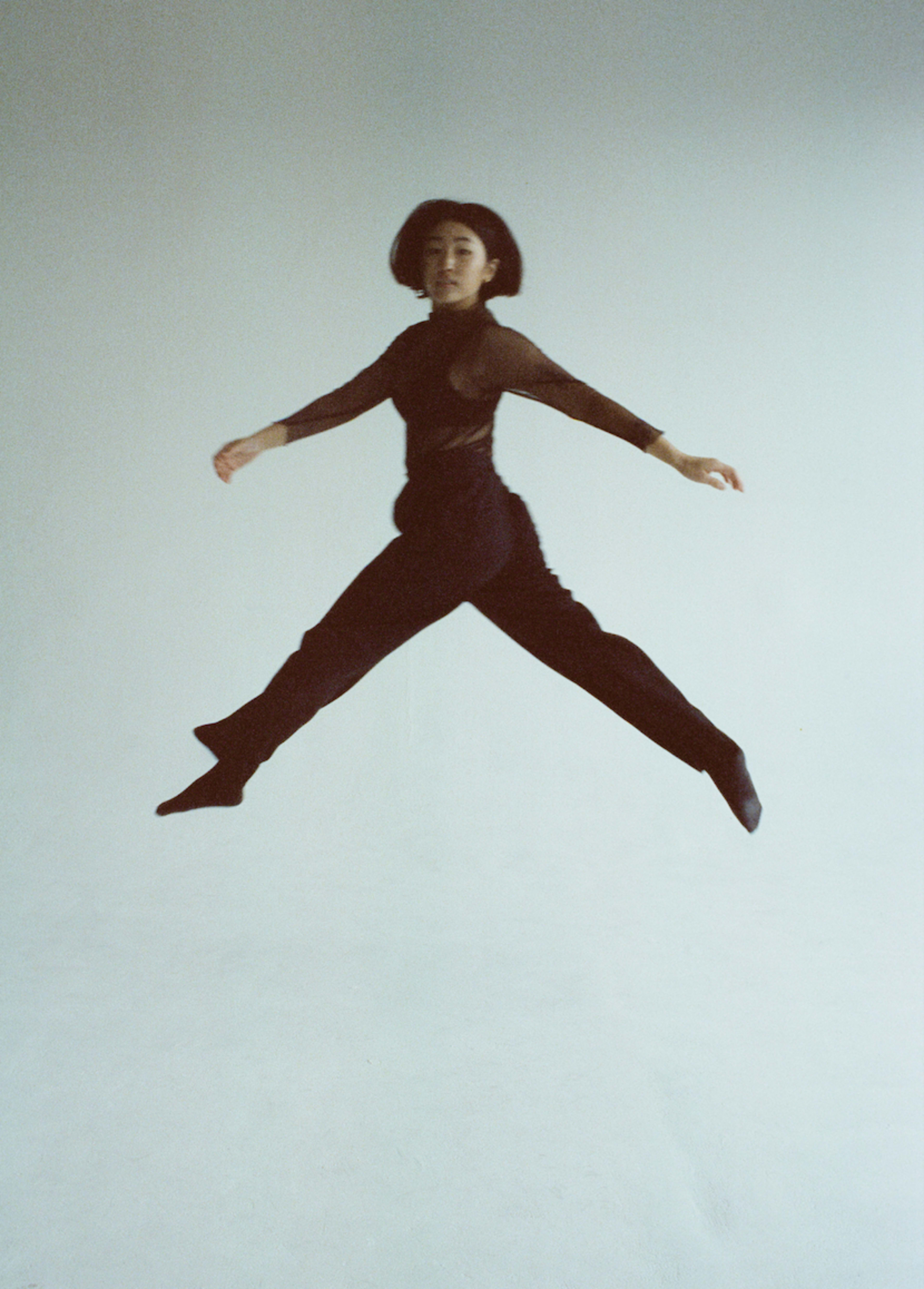 A woman in a black outfit is jumping during a photoshoot.