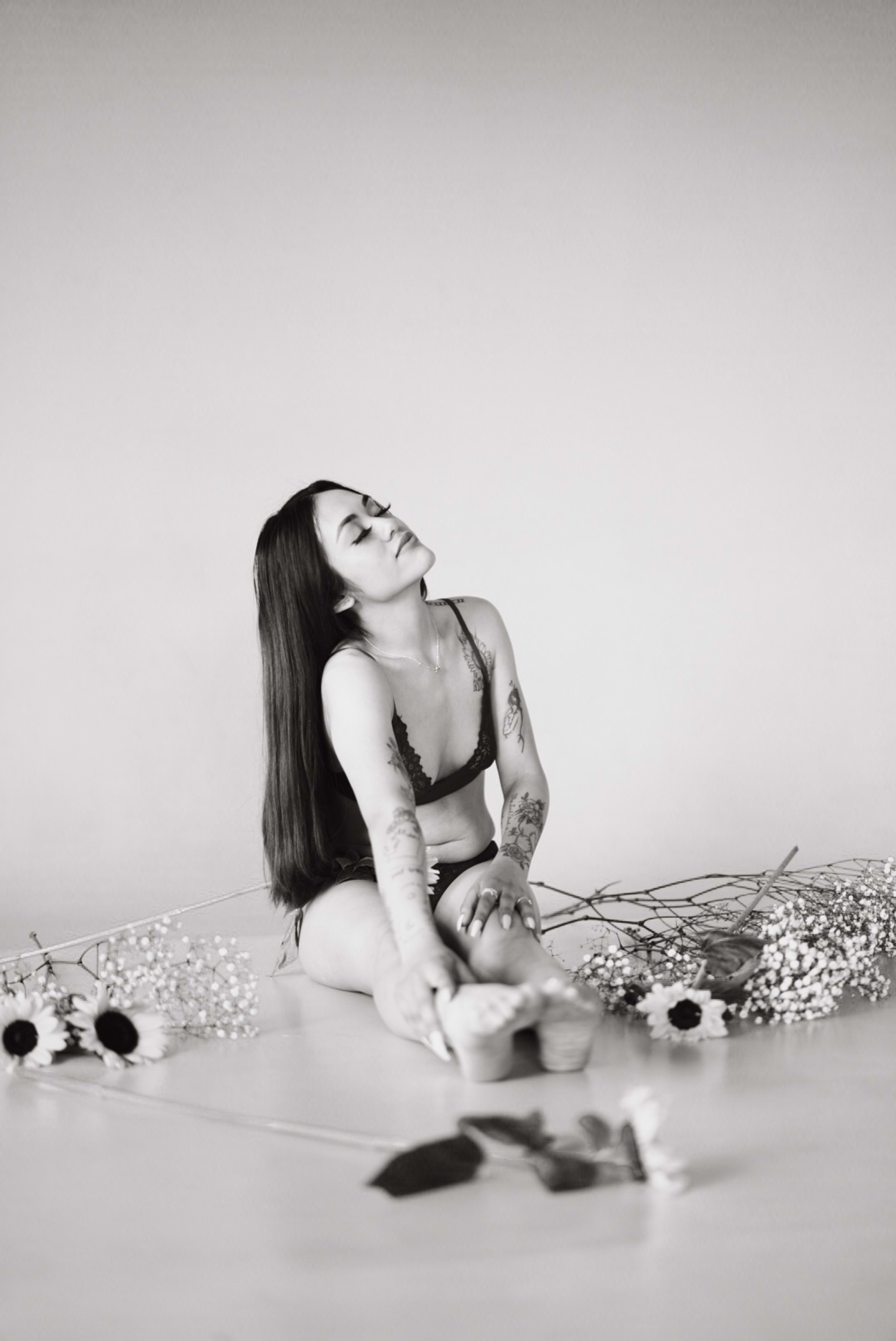 A boudoir photoshoot of a woman in black lingerie surrounded by sunflowers on the floor.