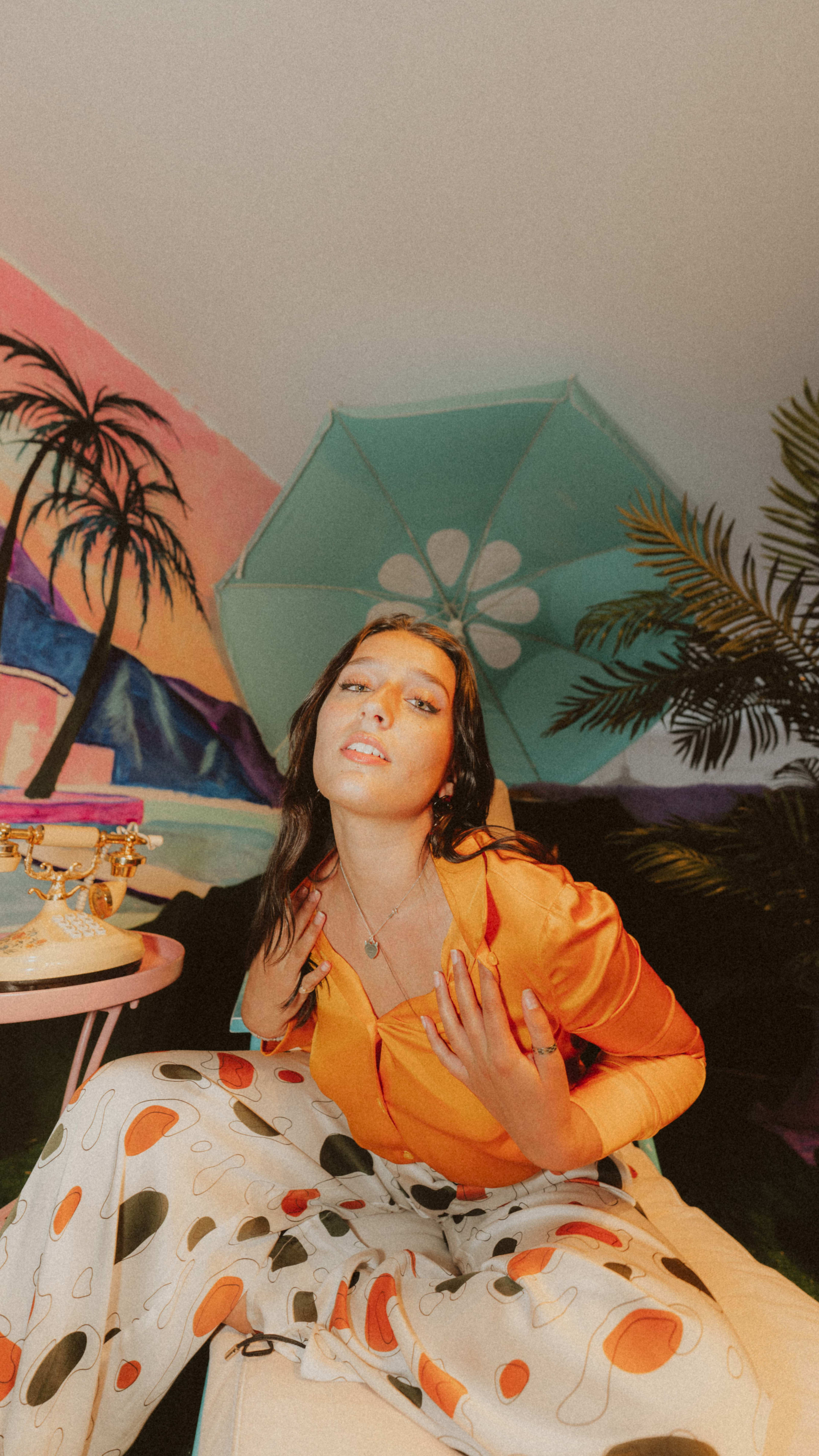 A retro photoshoot featuring a woman sitting with plants in the background.