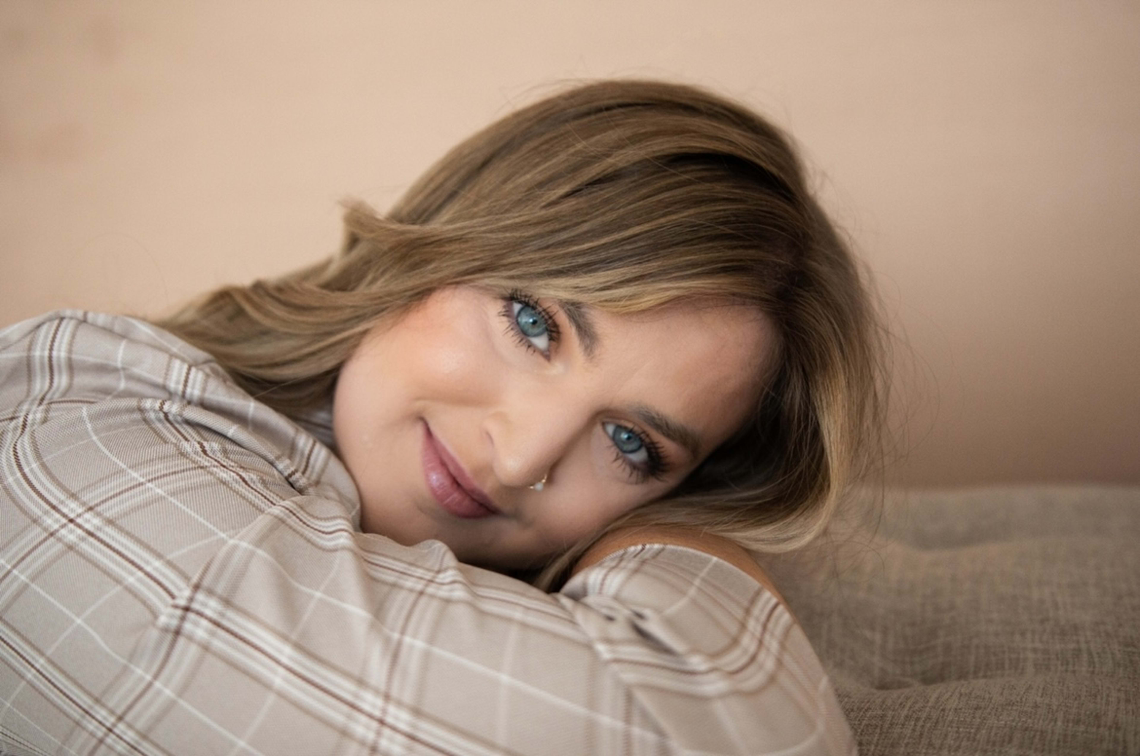 Portrait of a woman resting her head on her arm while on a light brown couch.