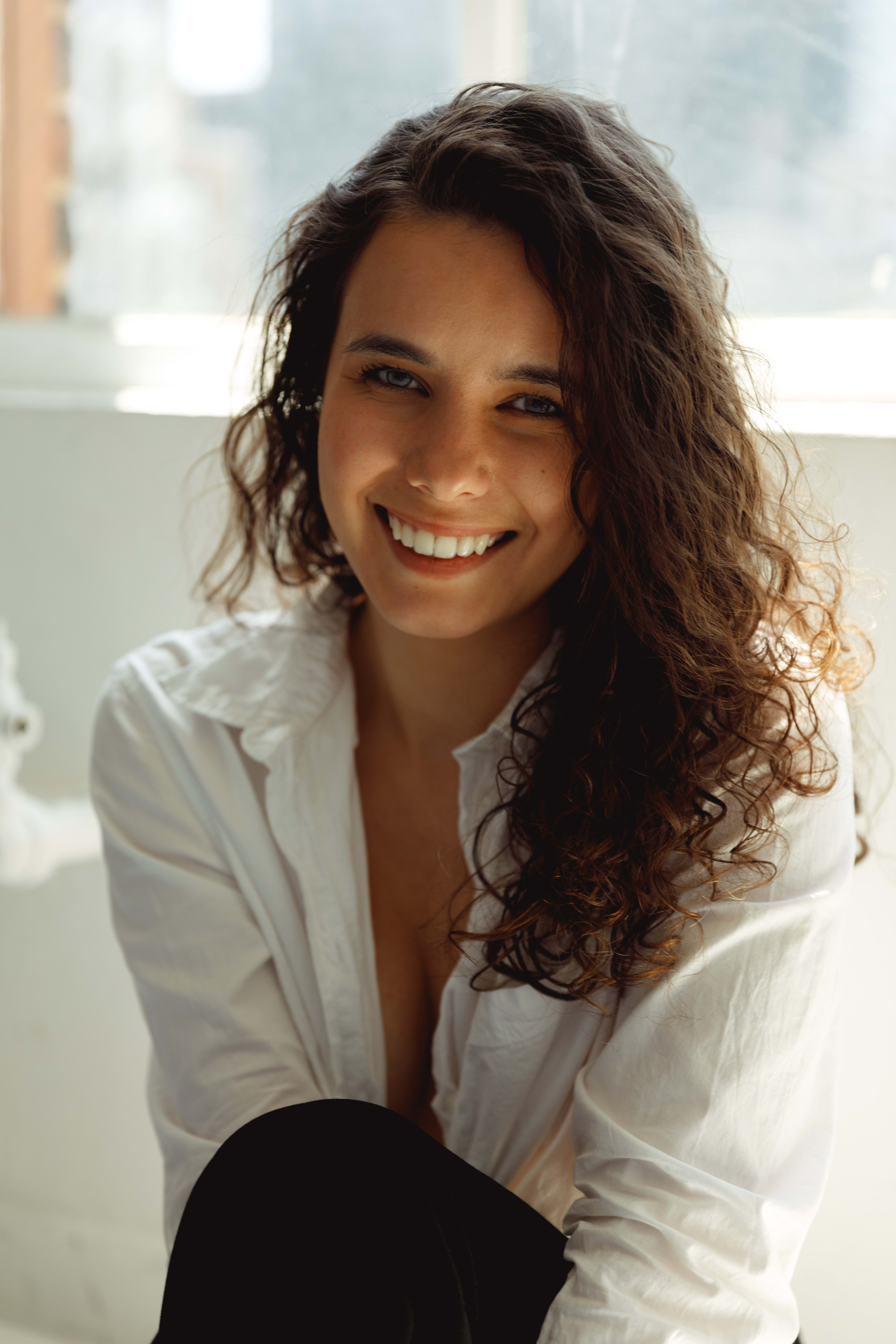 Retrato minimalista de una mujer con el pelo largo delante de una ventana blanca.