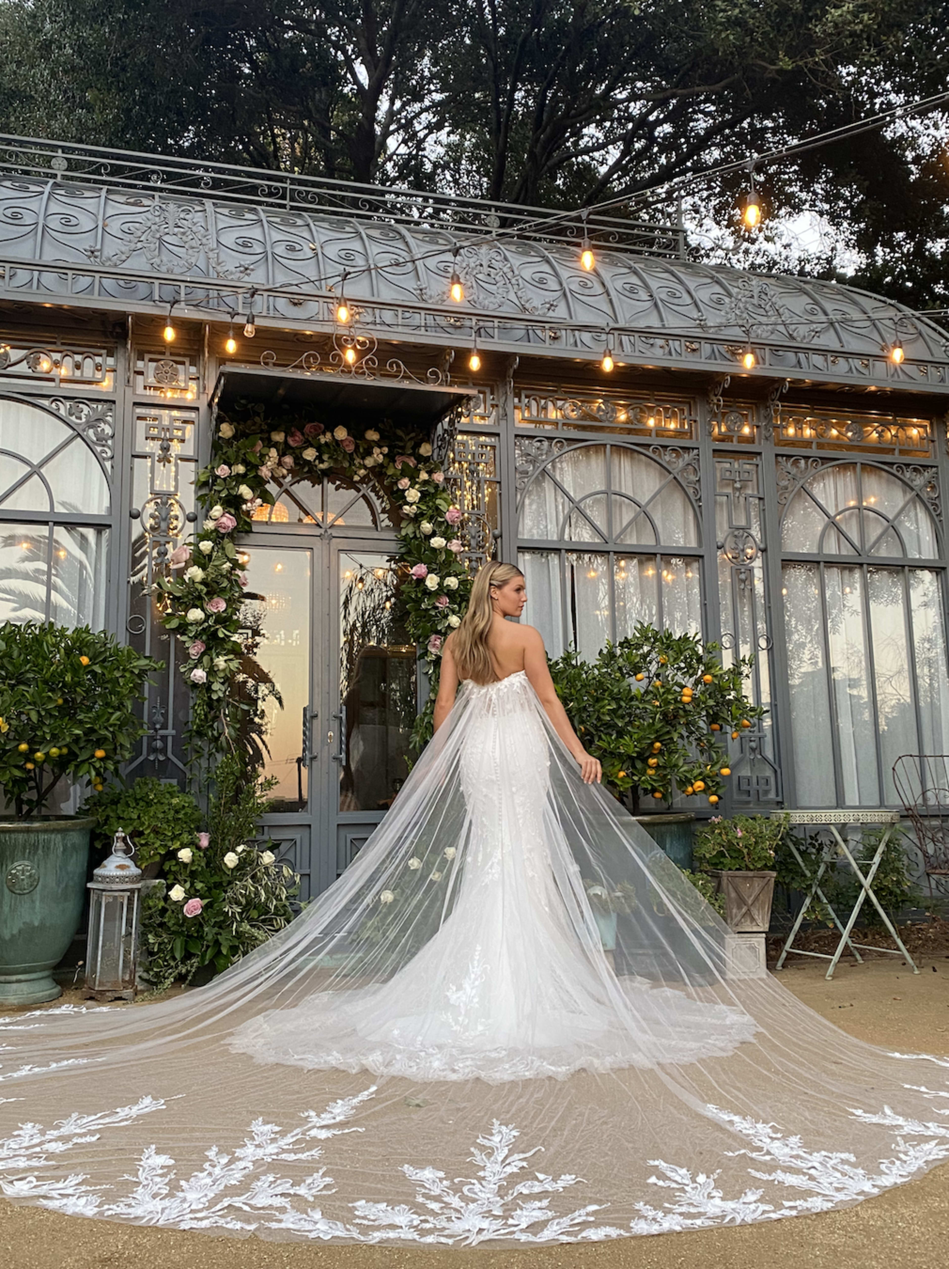 A bride posing for a photoshoot in a green garden wearing a white wedding dress.