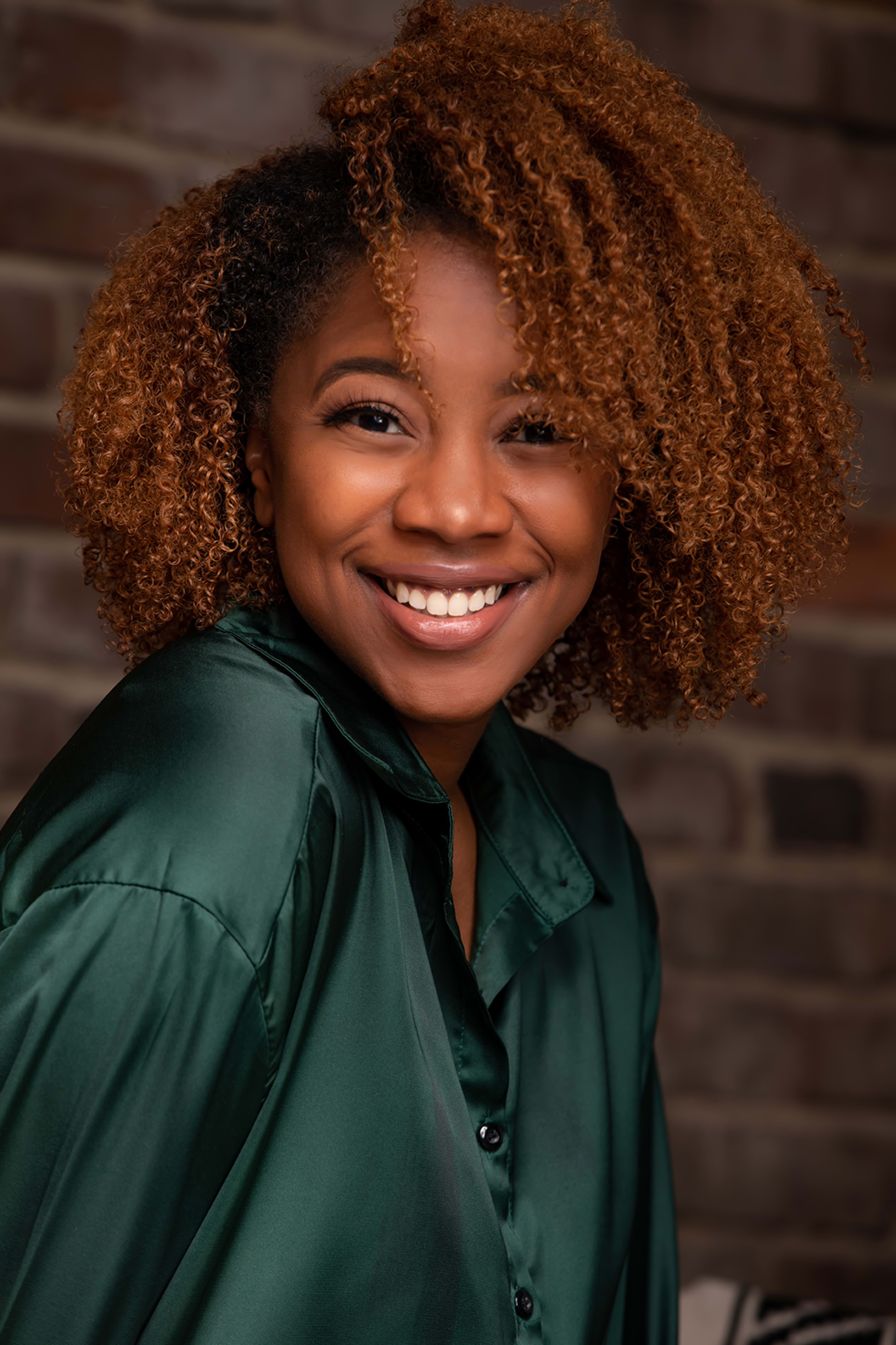 A woman with curly hair smiling for the camera for a portrait photo shoot.