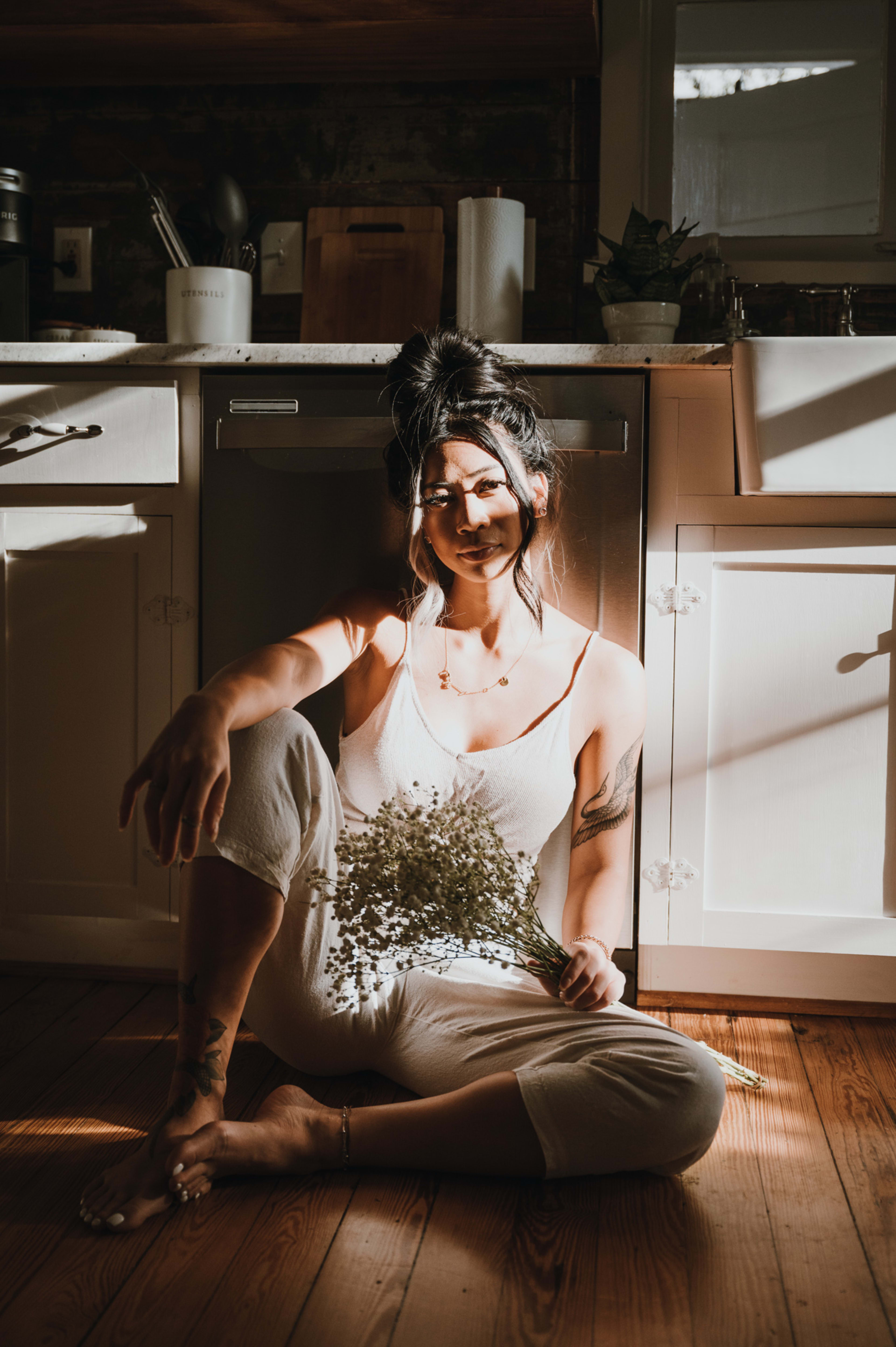 Eine weiße Frau sitzt während eines Modefotoshootings auf dem Boden und hält eine Pflanze in der Hand.