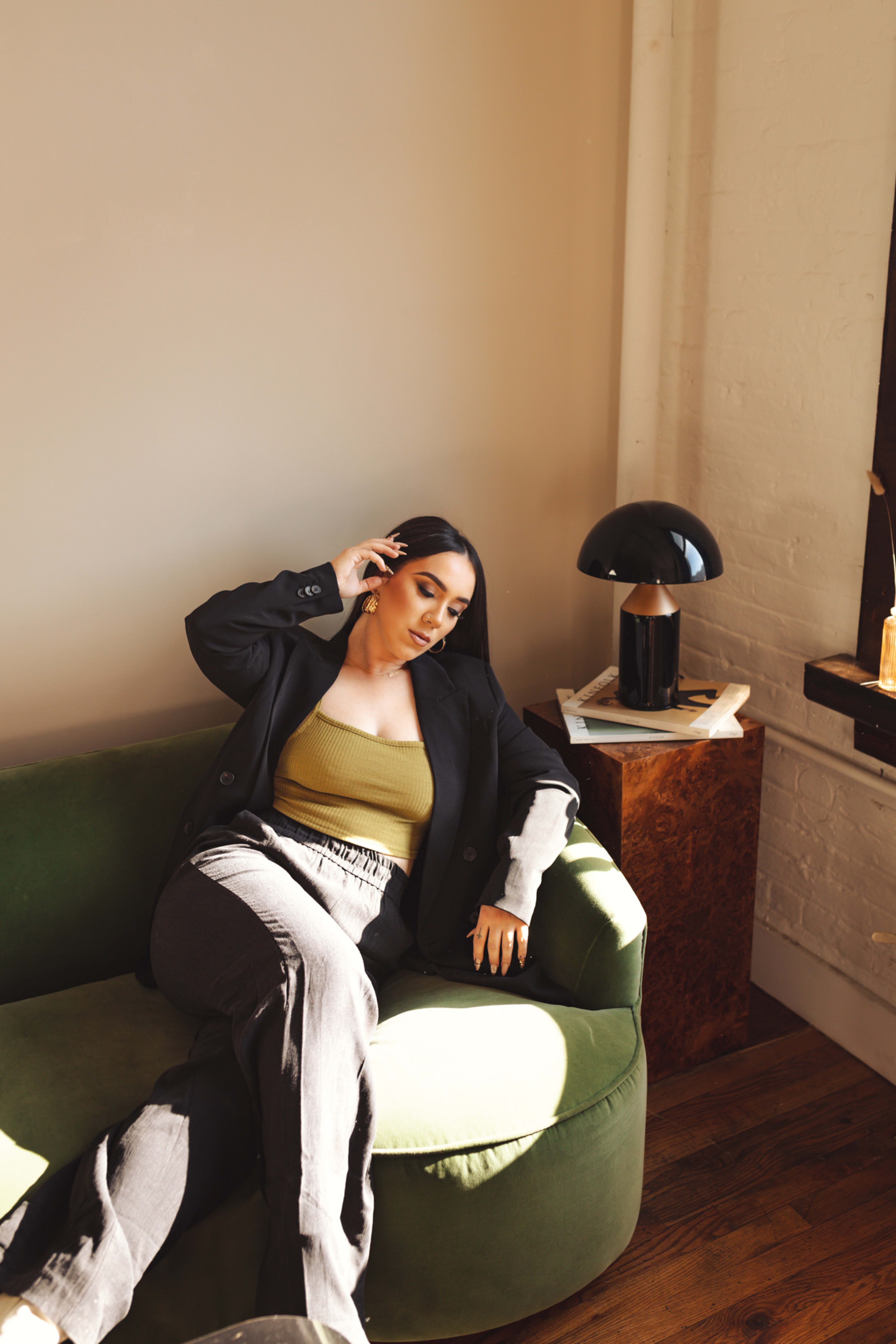 A fashion photoshoot featuring a woman posing on a green couch in a white room.