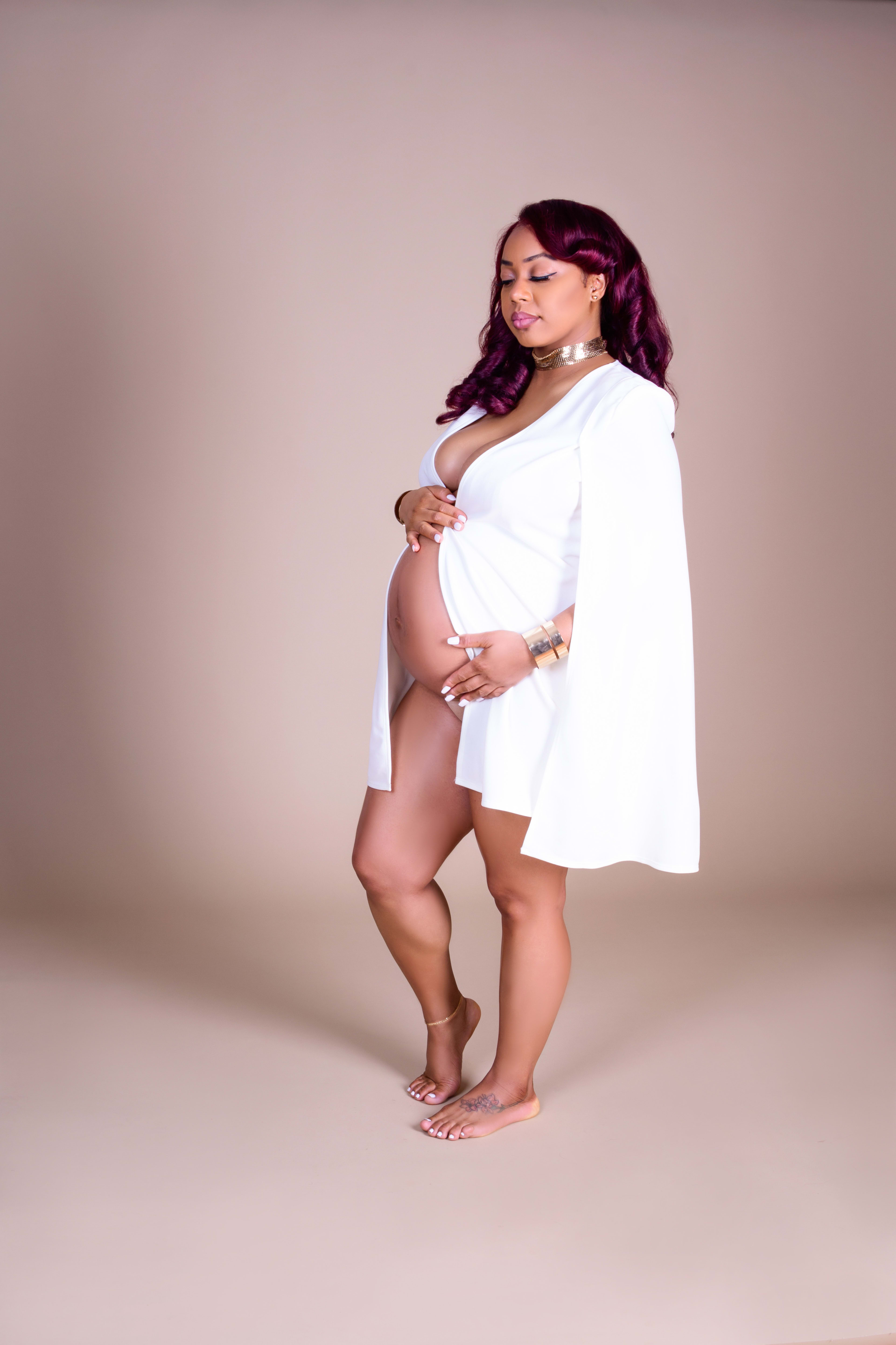 A pregnant woman in a white dress posing for a maternity photoshoot.