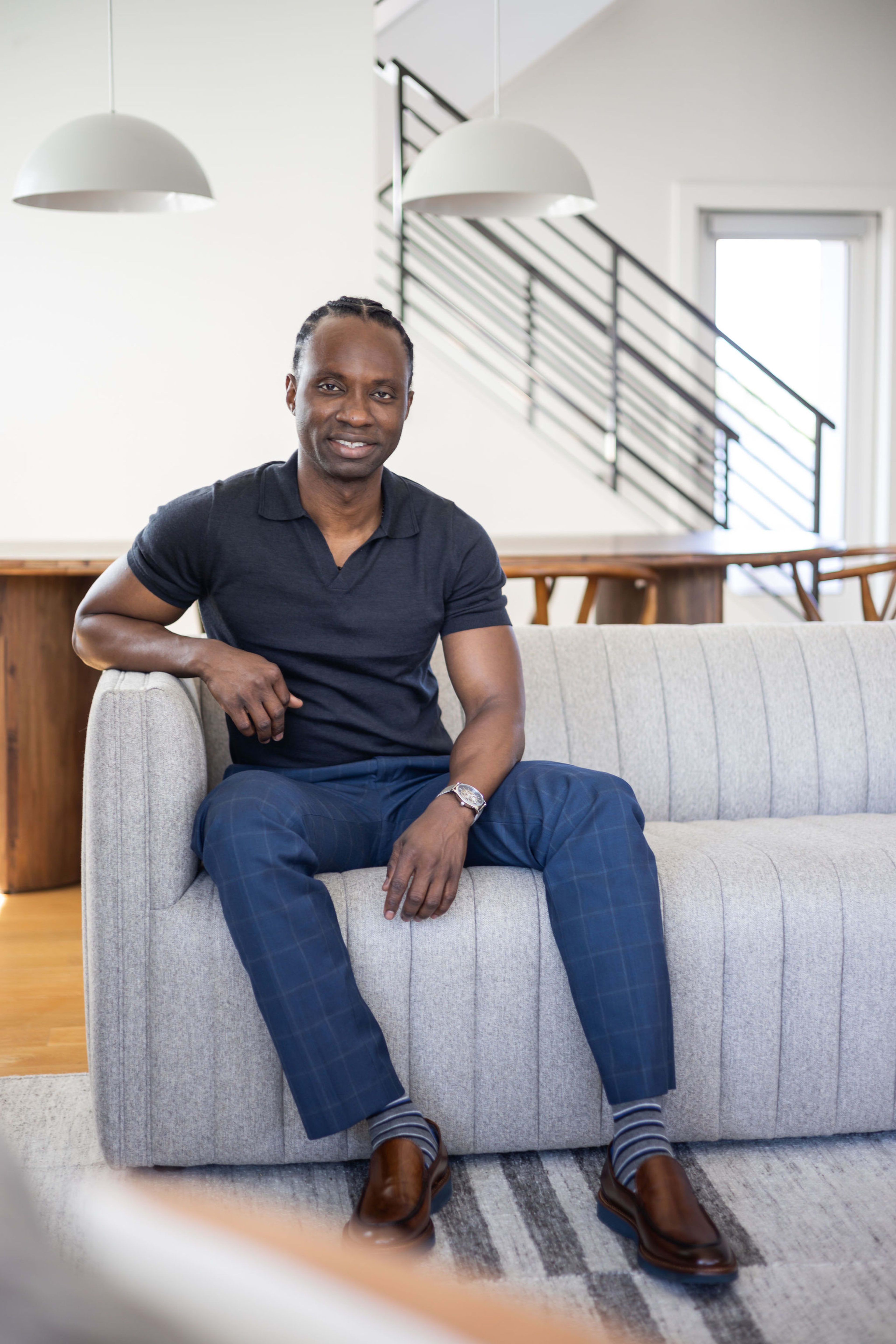 A photoshoot of a man sitting on a couch in a white living room.