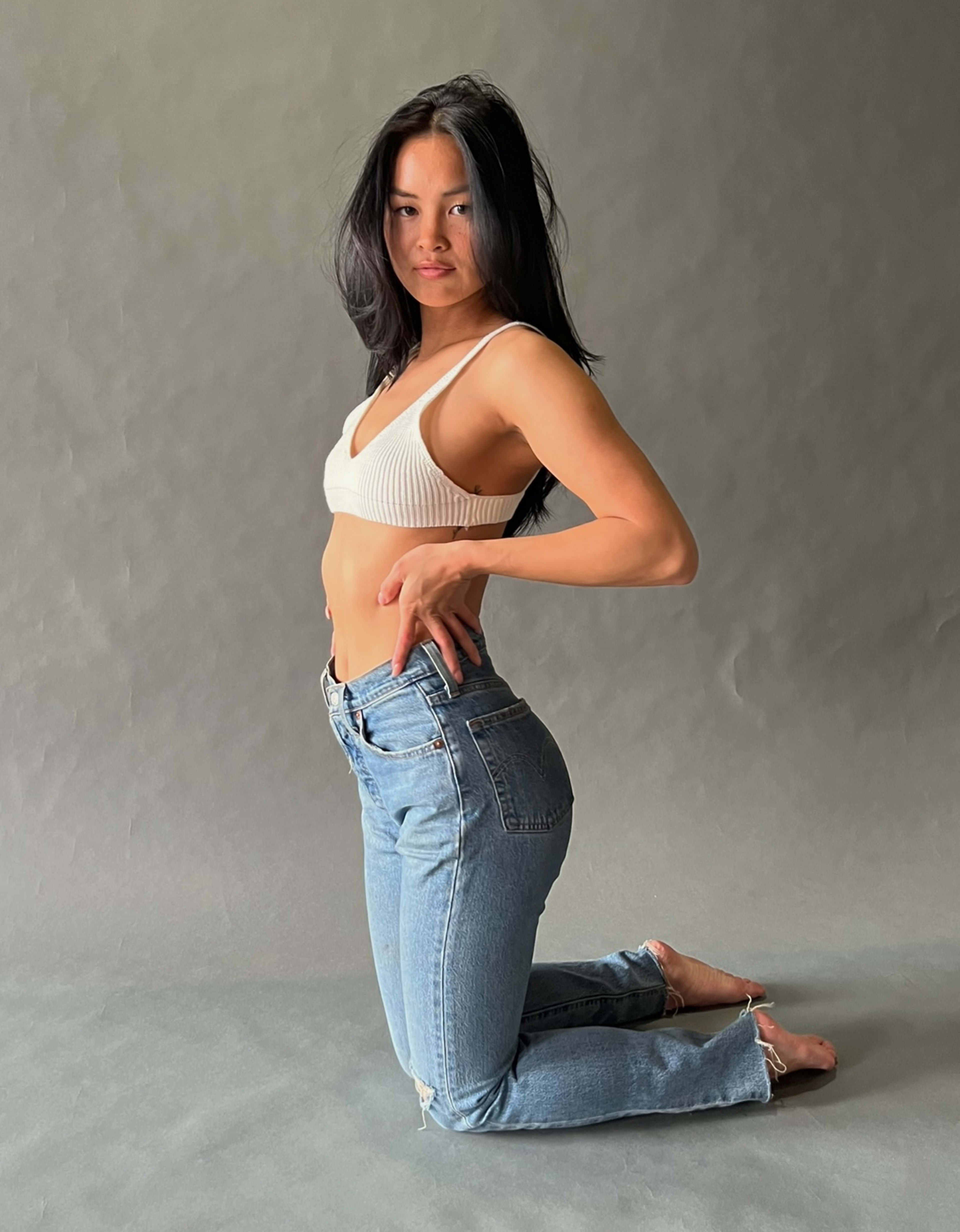 A minimal photoshoot of a woman sitting on the ground with her hands on her hips in blue and grey tones.