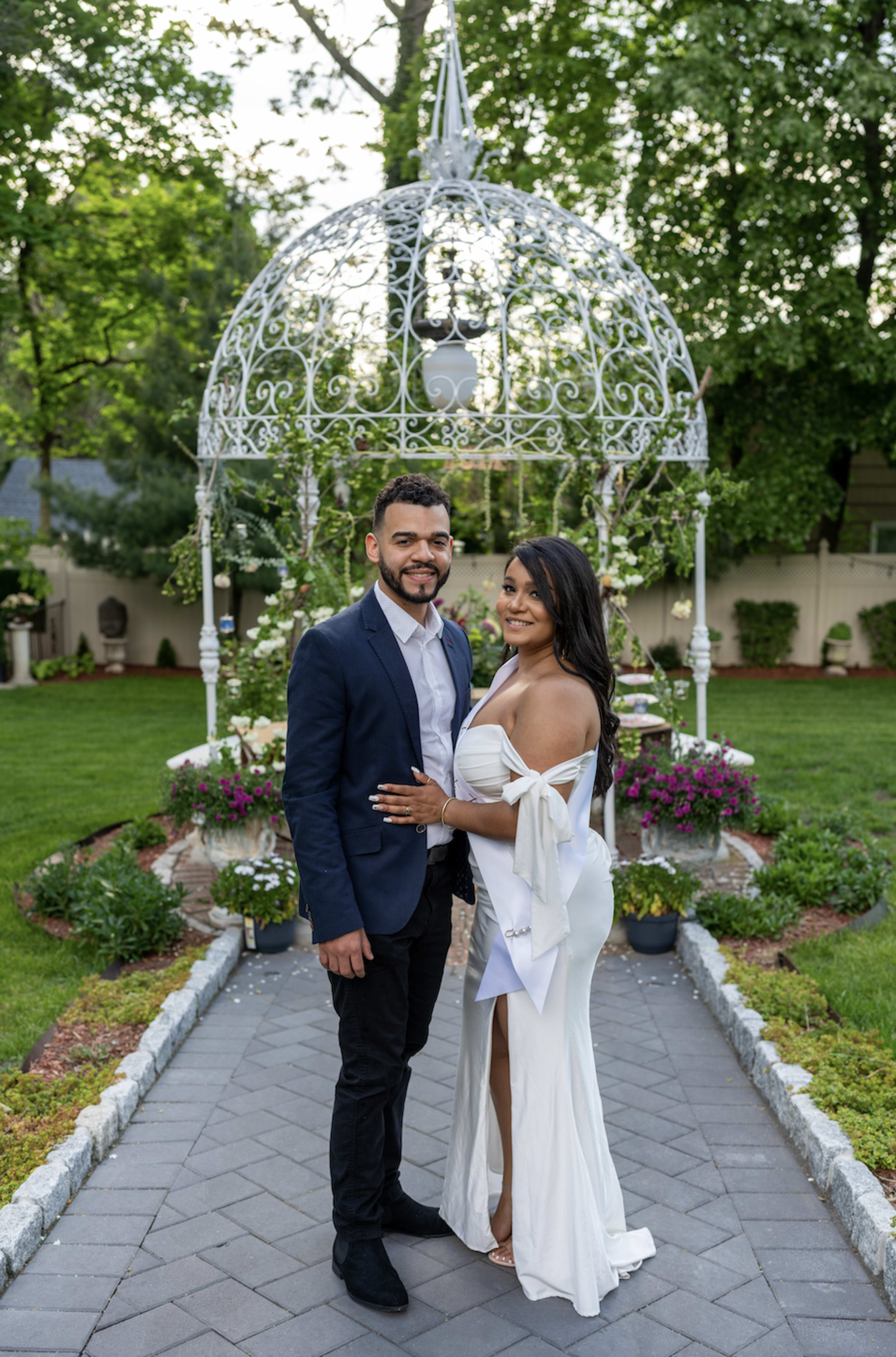 A couple posing for an outdoor photoshoot in front of a white gazebo.