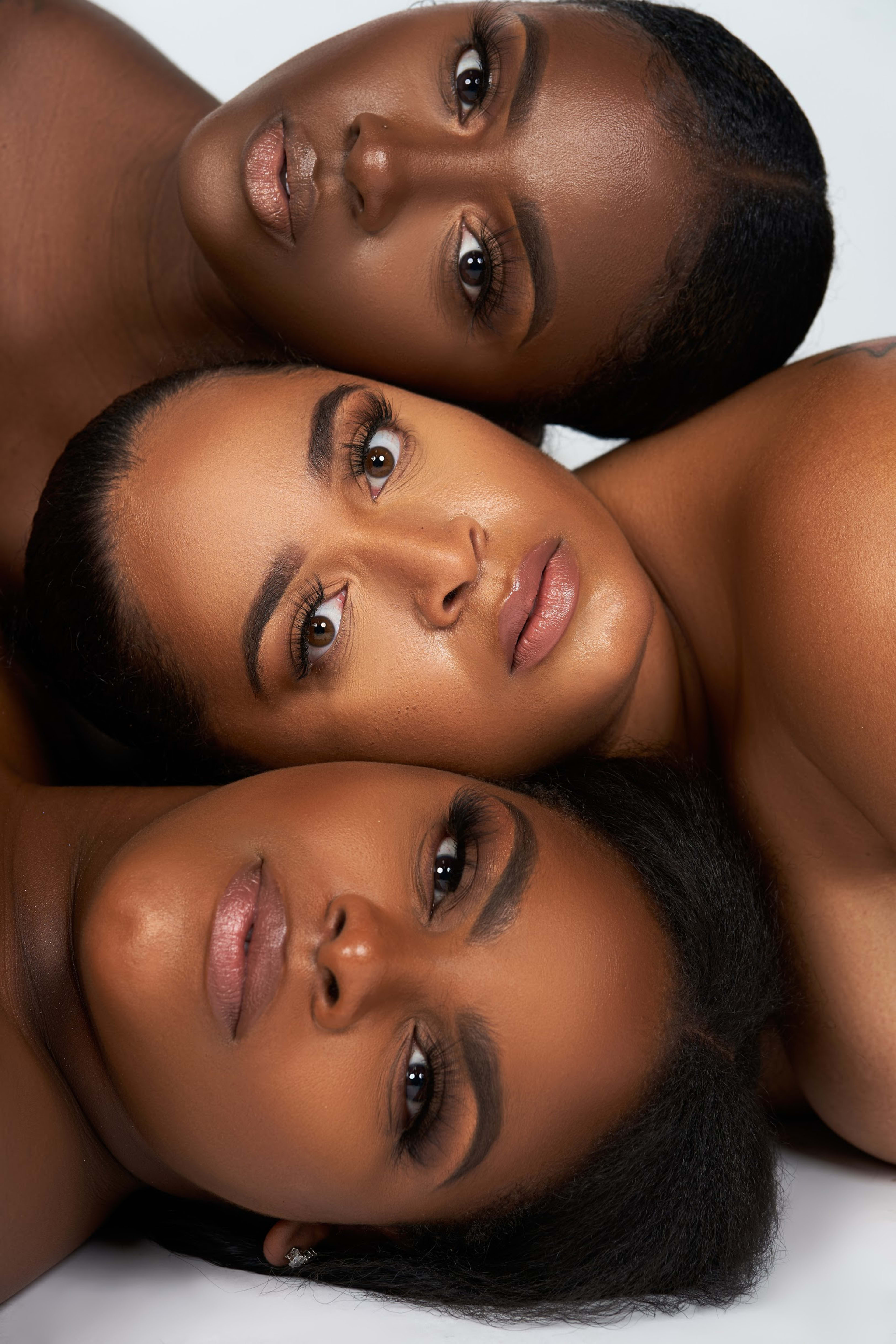 A trio of females posing for a photoshoot, lying side-by-side.