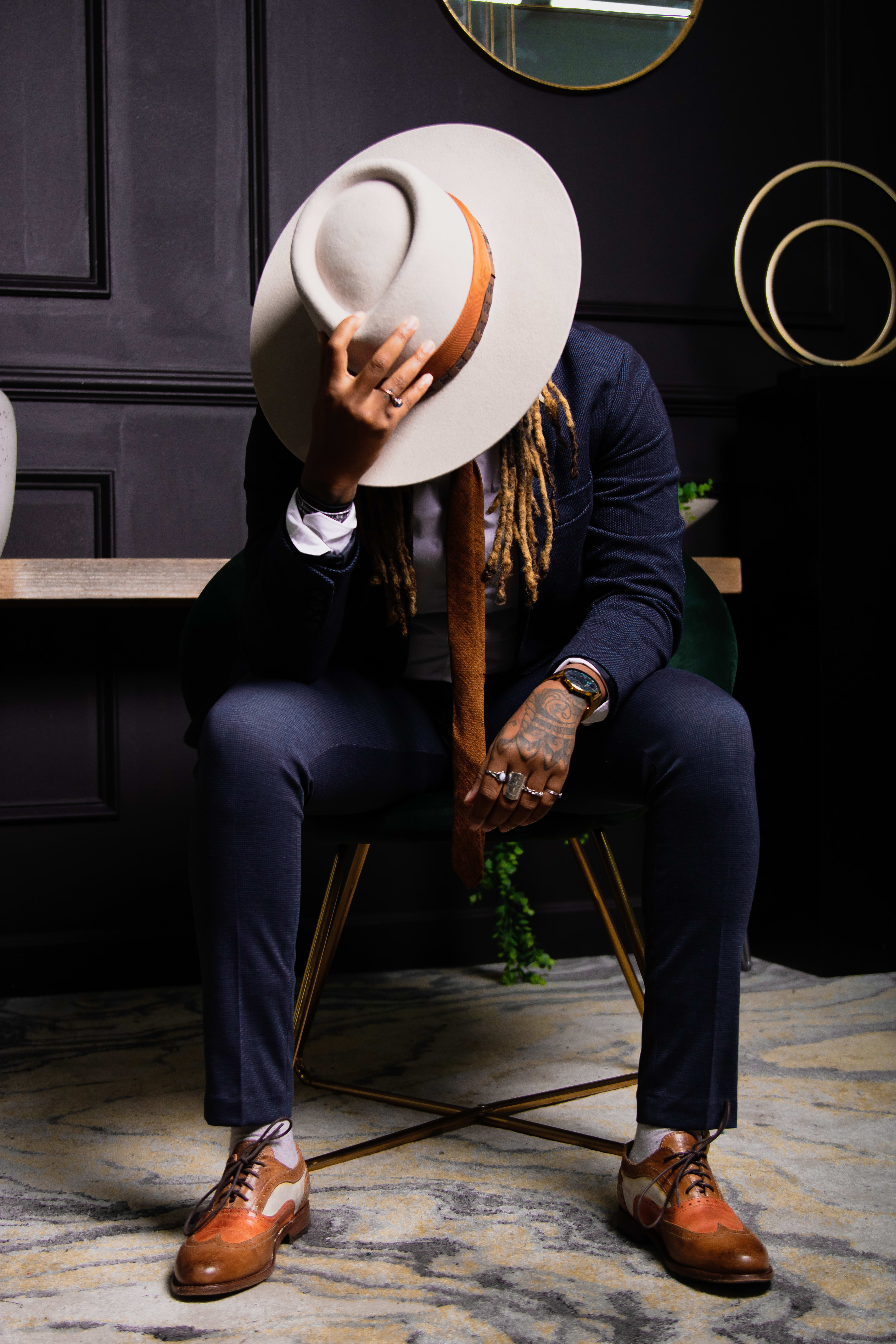A man in a fashionable white hat and blue suit poses confidently for a photo shoot.