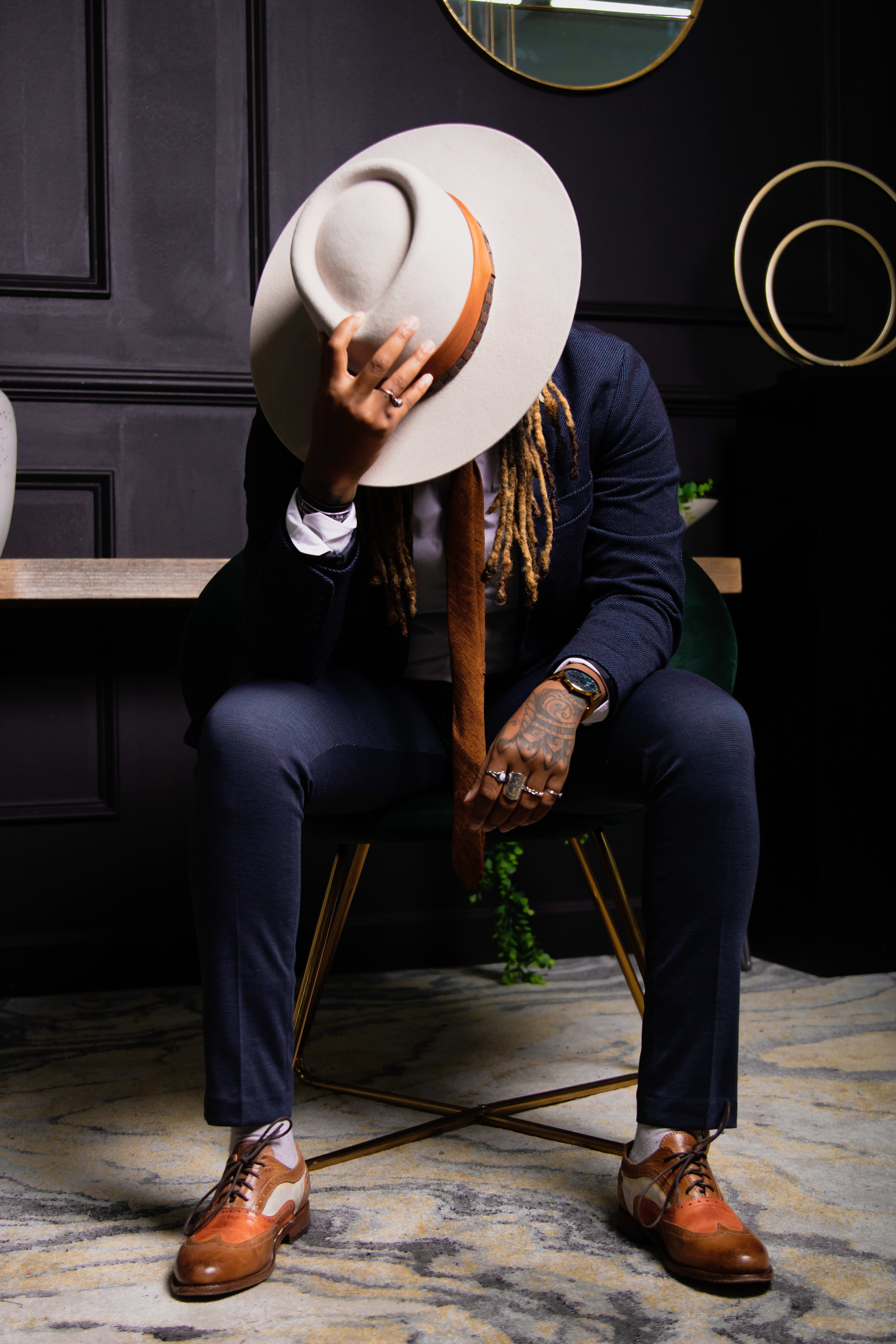 Un hombre con un sombrero blanco de moda y un traje azul posa con confianza para una sesión de fotos.