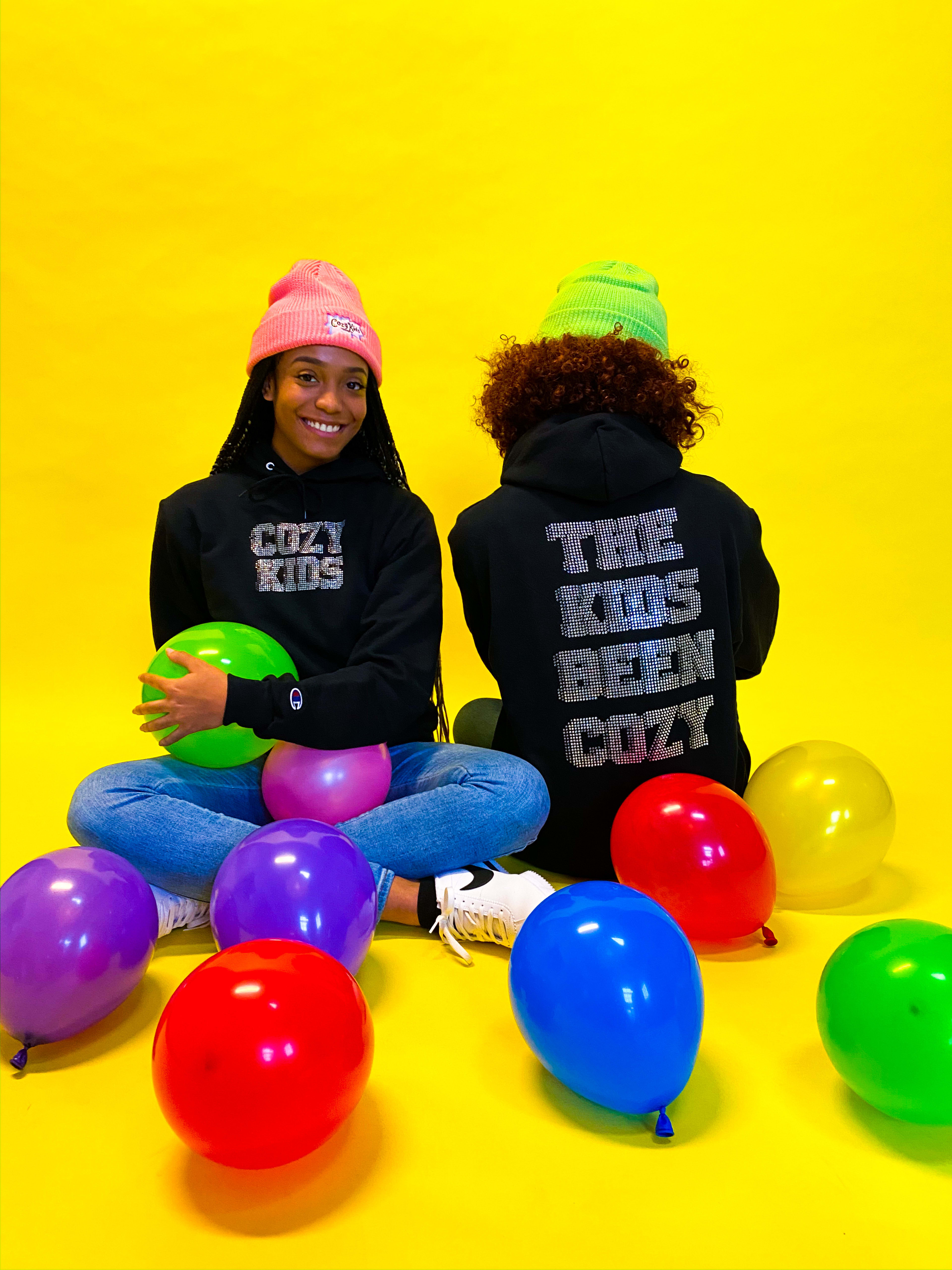 Two people sitting on the ground with rainbow balloons.