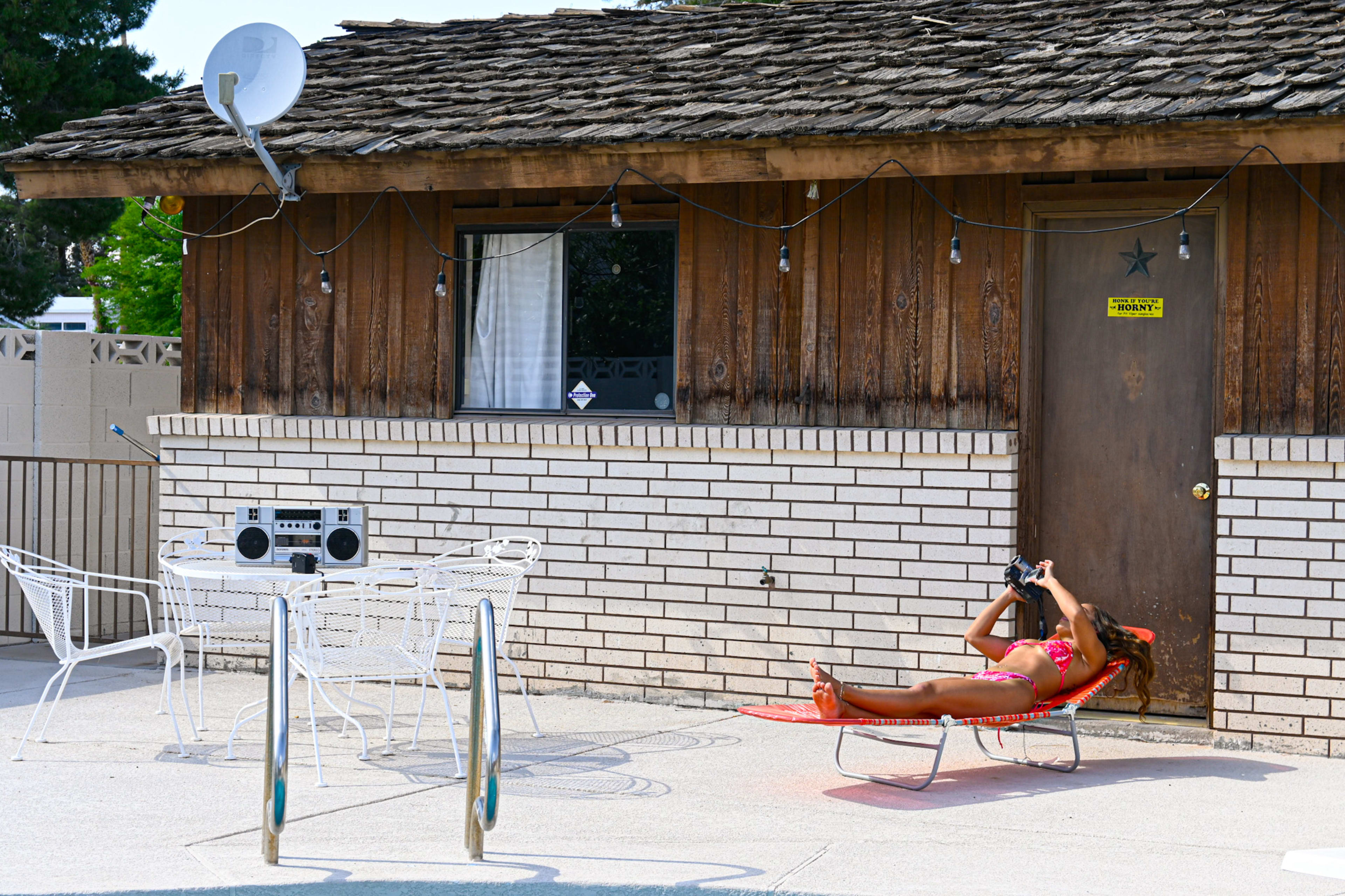 A woman in a bikini relaxing on a lawn chair outside of a rustic house.