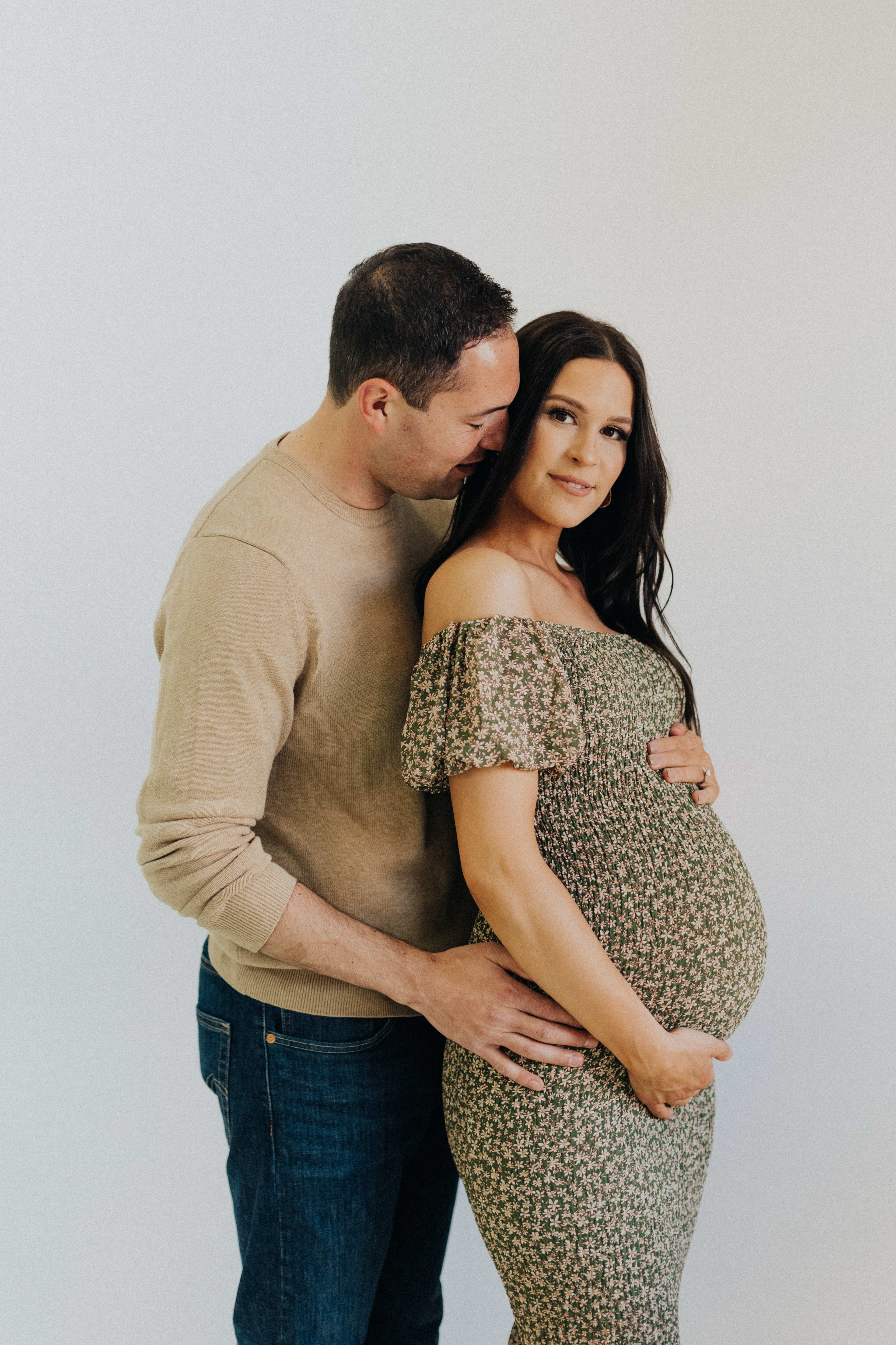 A pregnant woman and a man posing for a minimal beige maternity photoshoot.