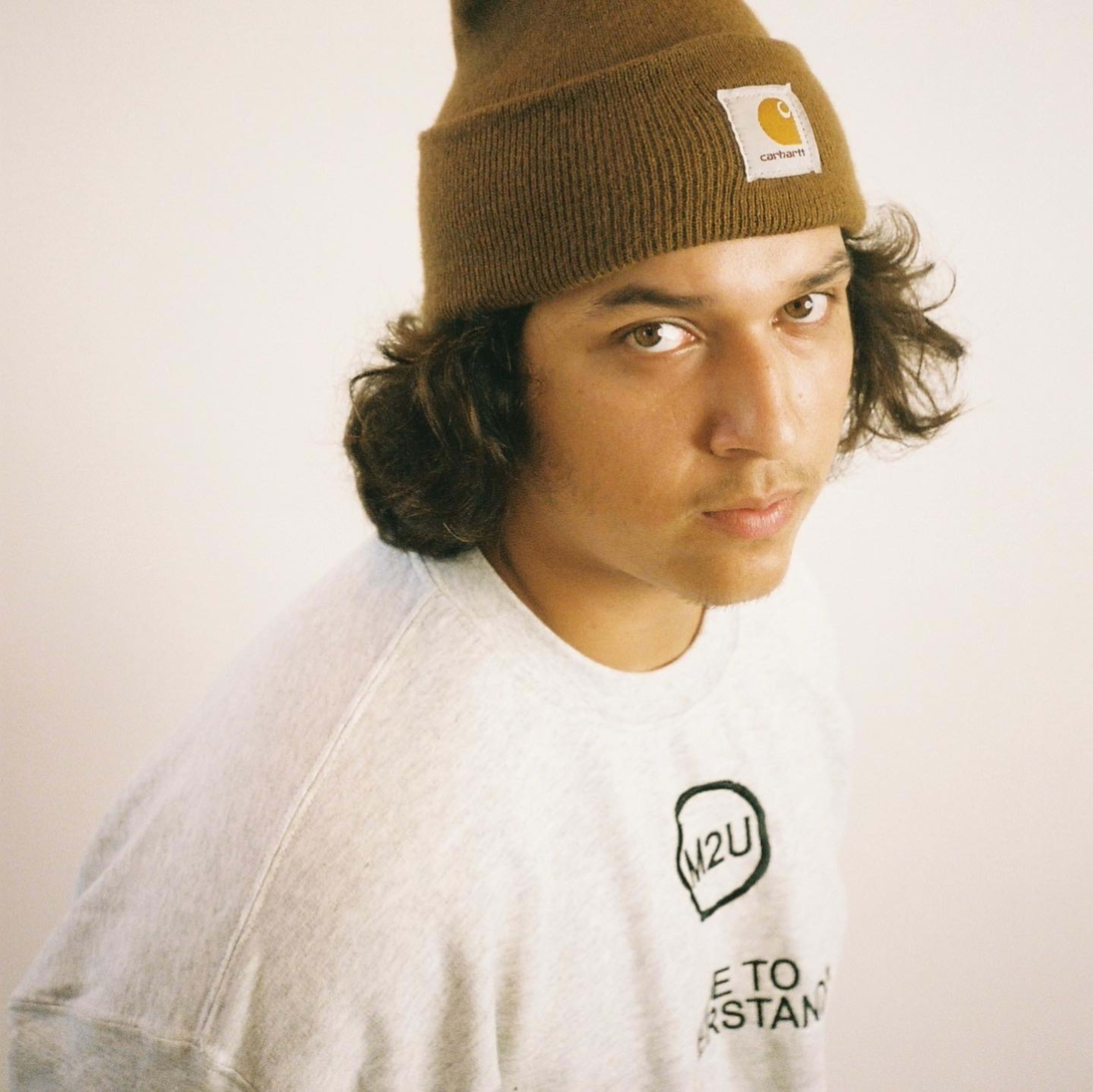 A young man, wearing a beanie, poses for a white portrait head shot.