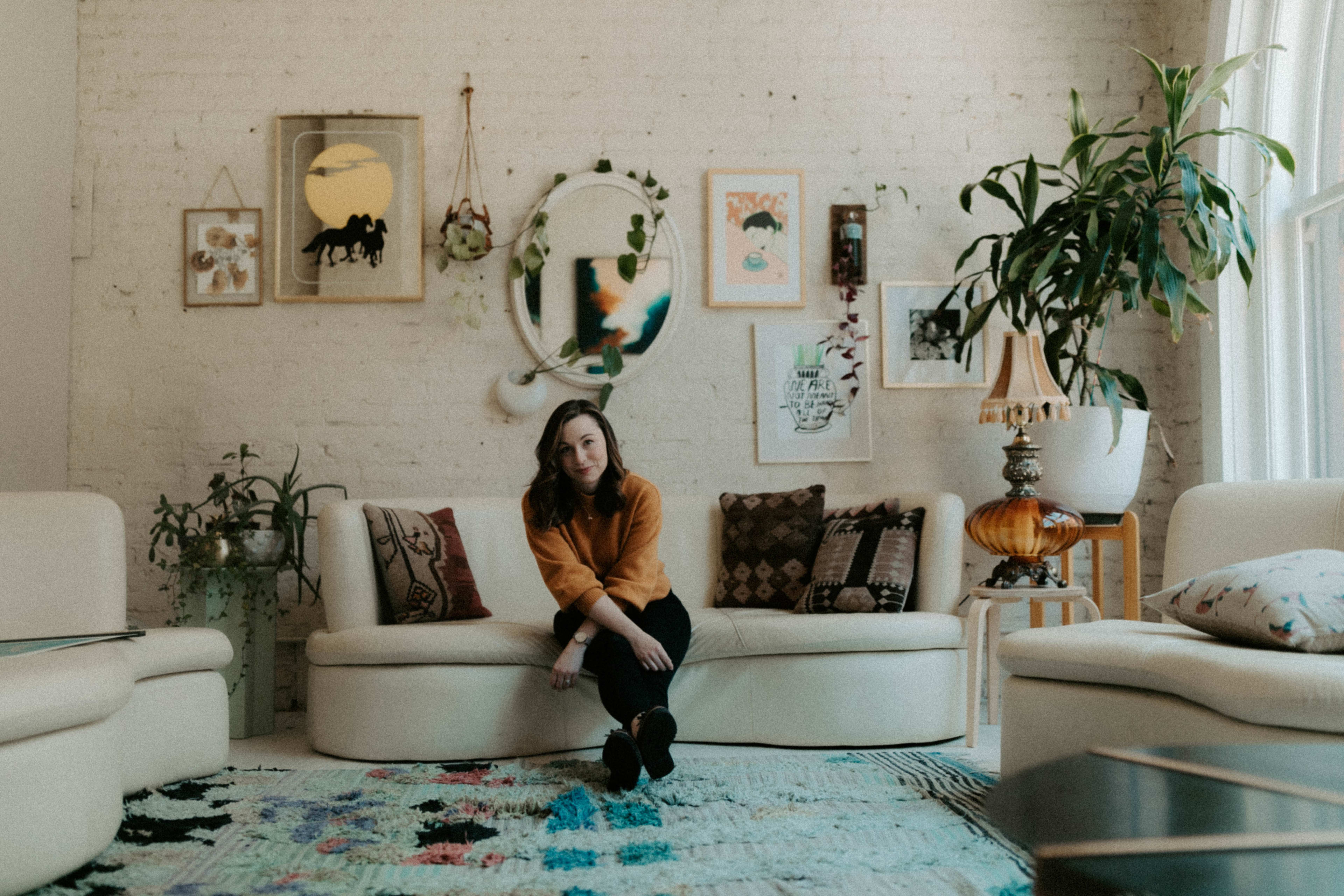 A woman lounging on a rustic couch surrounded by leafy plants in her living room.