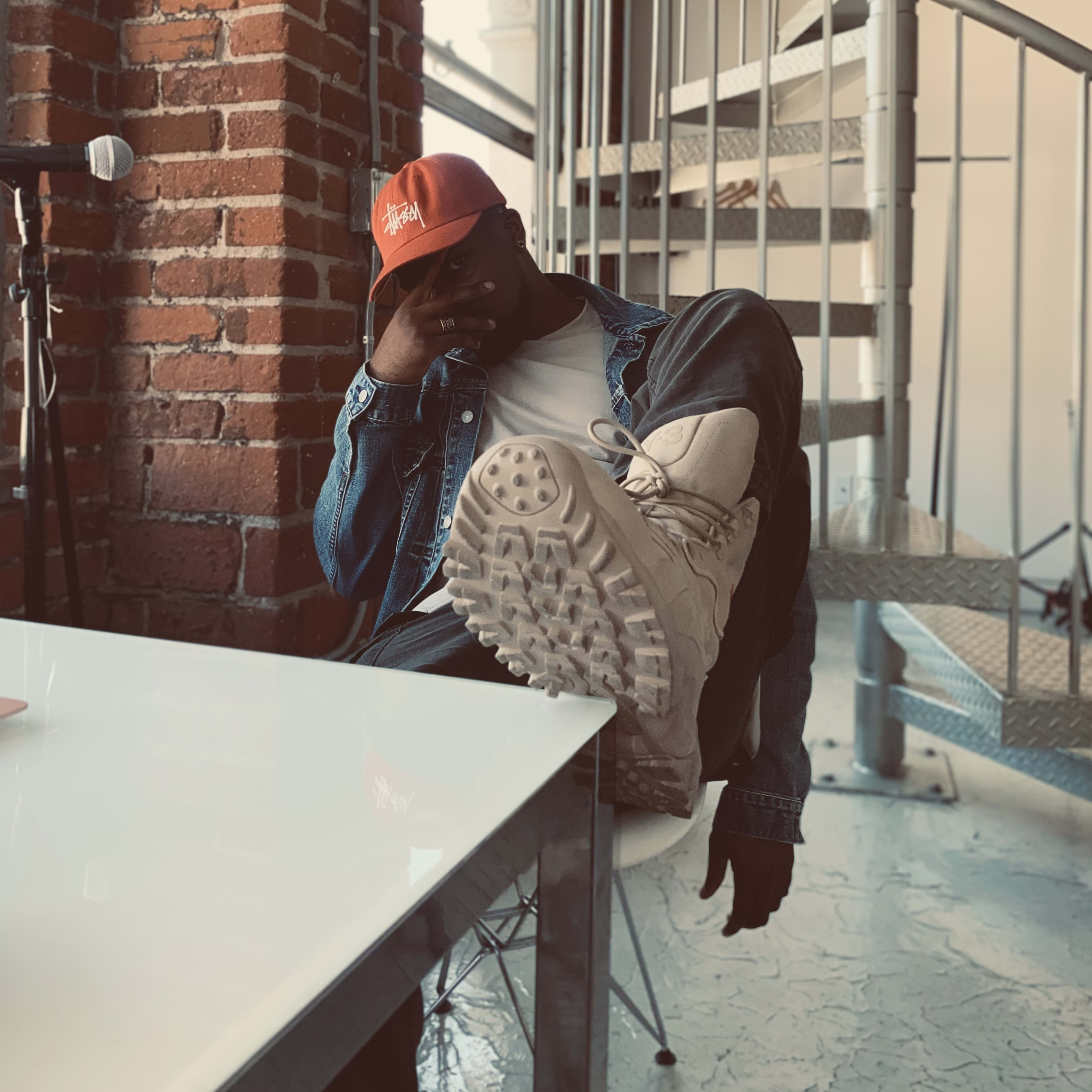 A fashion model posing on a white counter against a brick wall during a photoshoot.