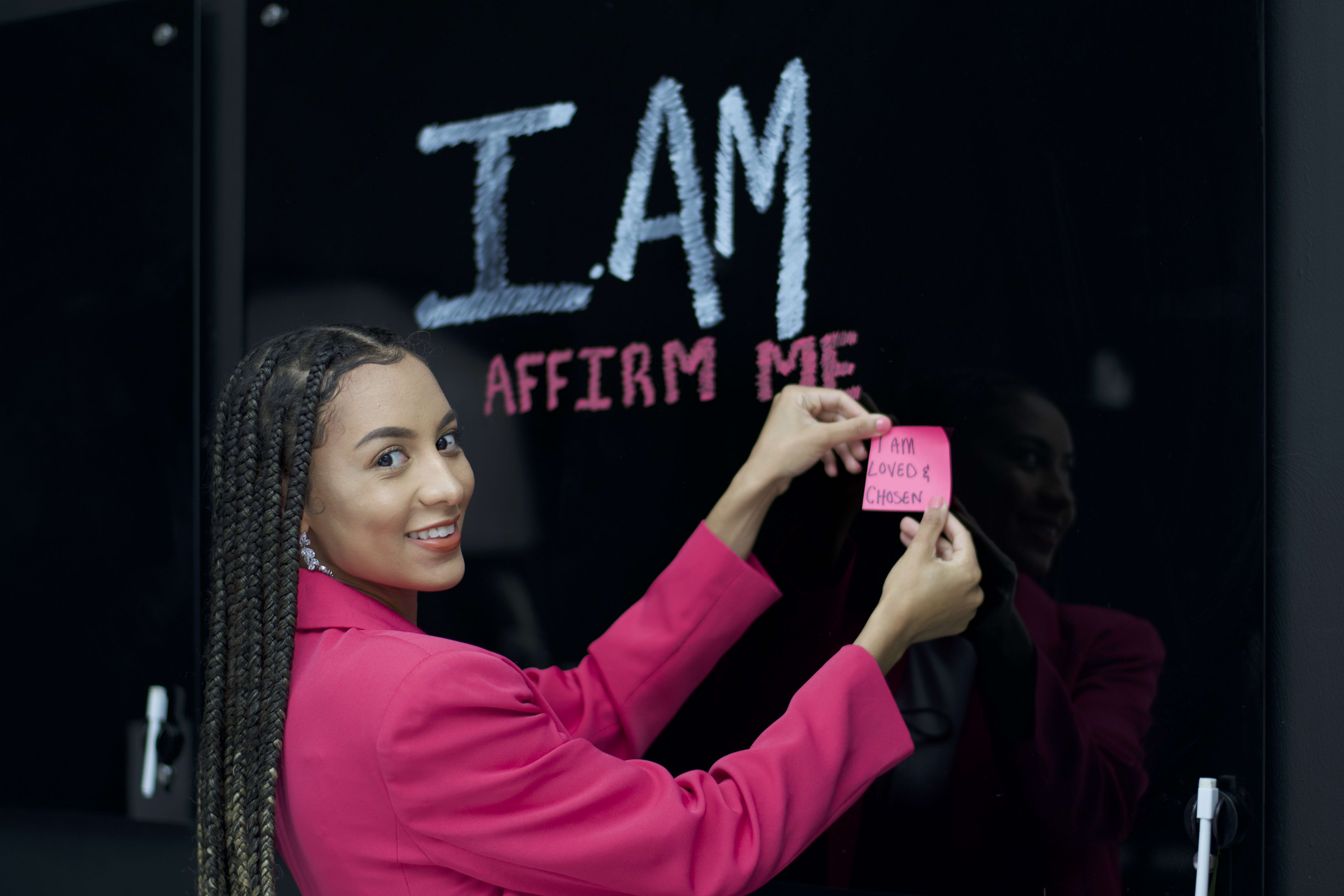 A woman in a photoshoot wearing a pink shirt, in front of a black wall.