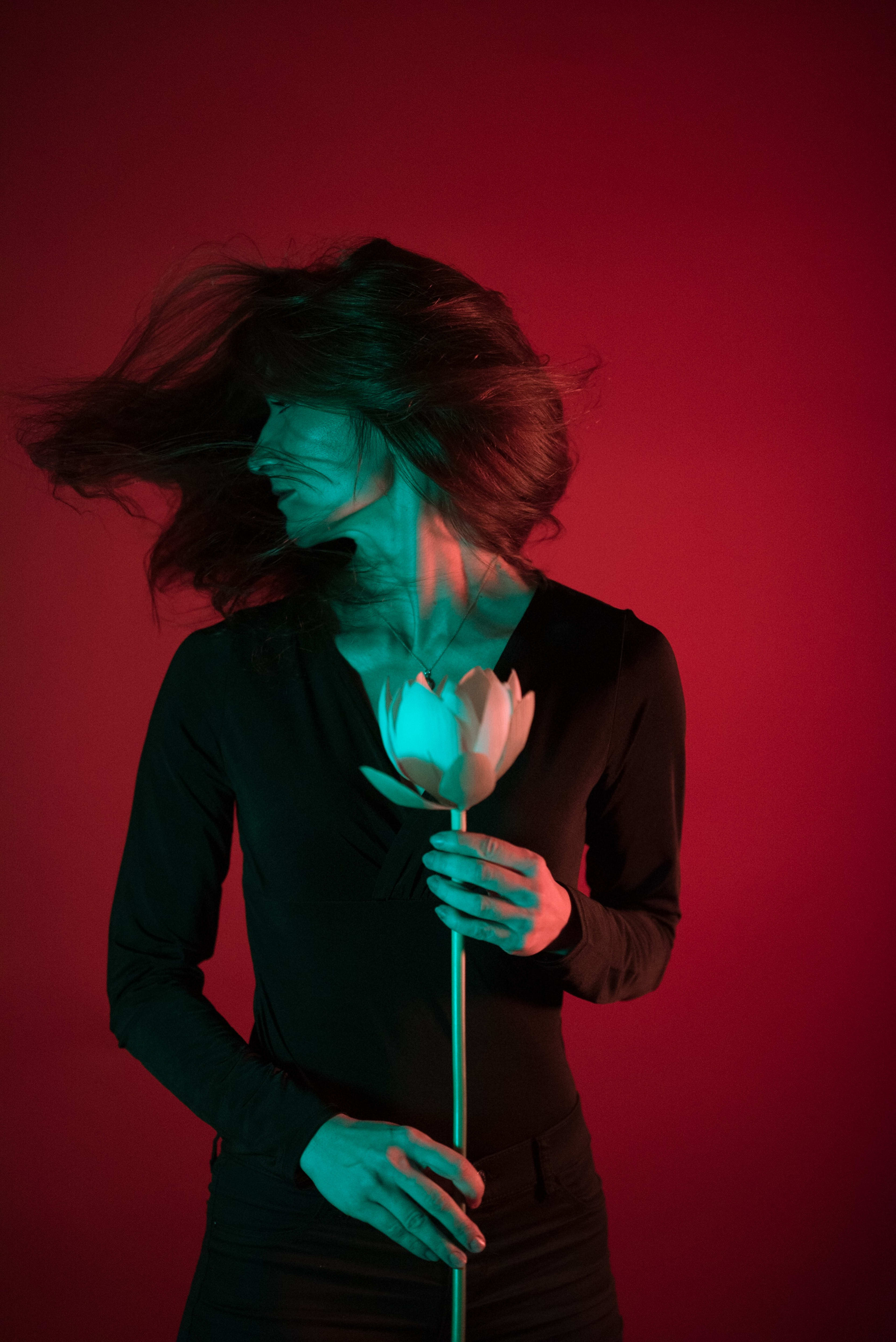 A woman with long dark hair holding a flower on a red background.