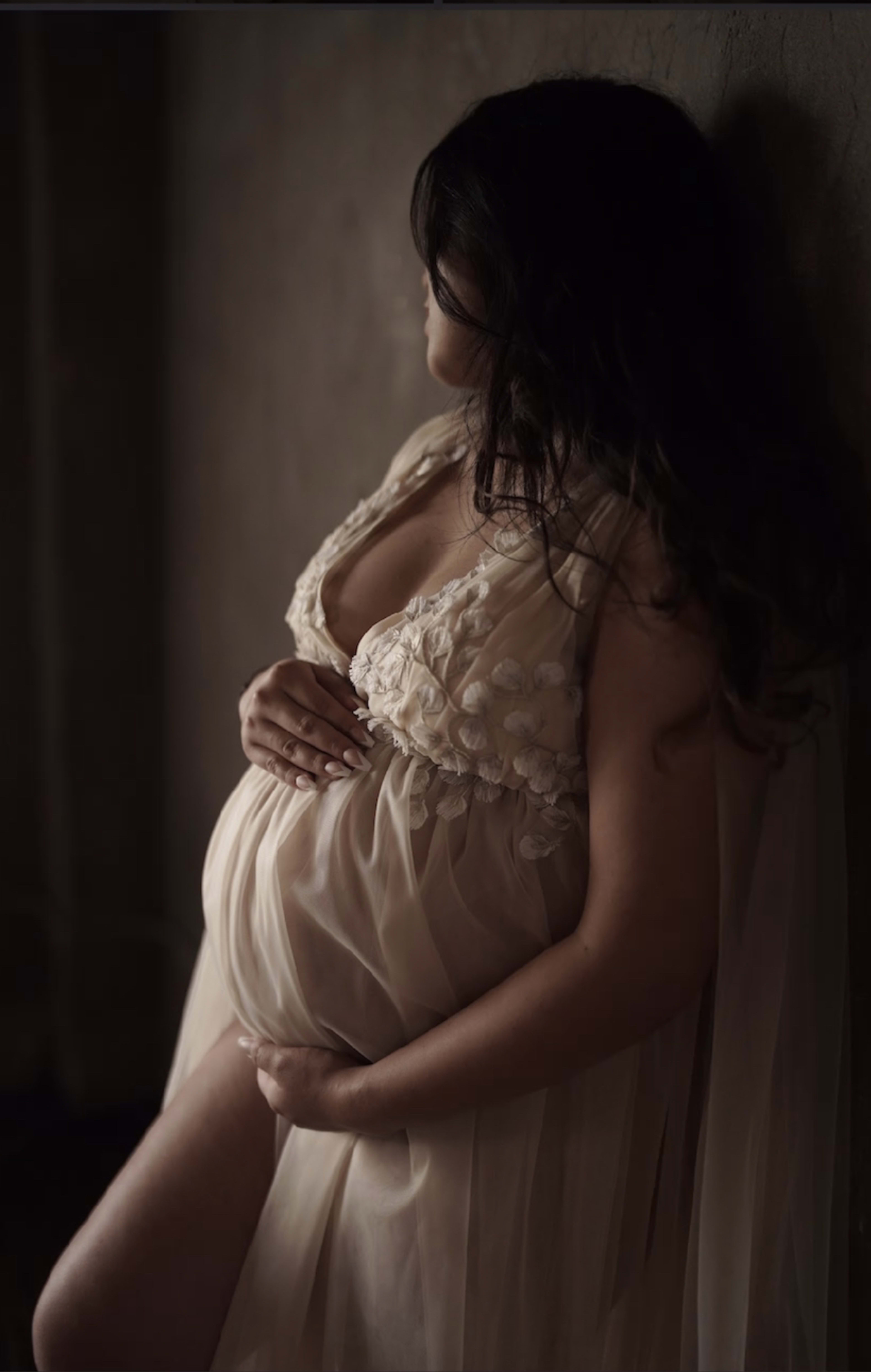 A pregnant woman in a beige dress poses for a maternity photo shoot.