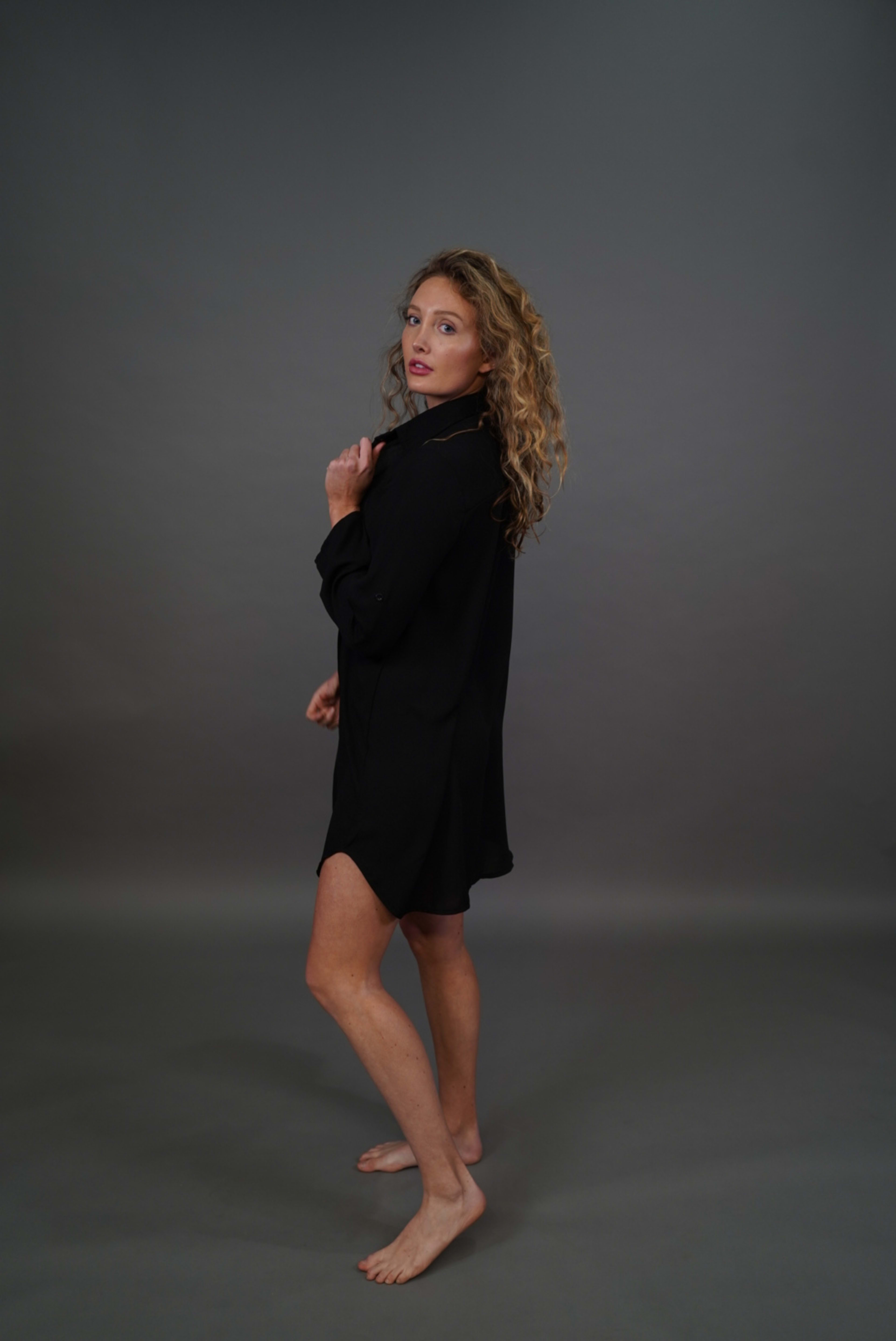 A woman in a long black shirt posing for a minimalist photo shoot.