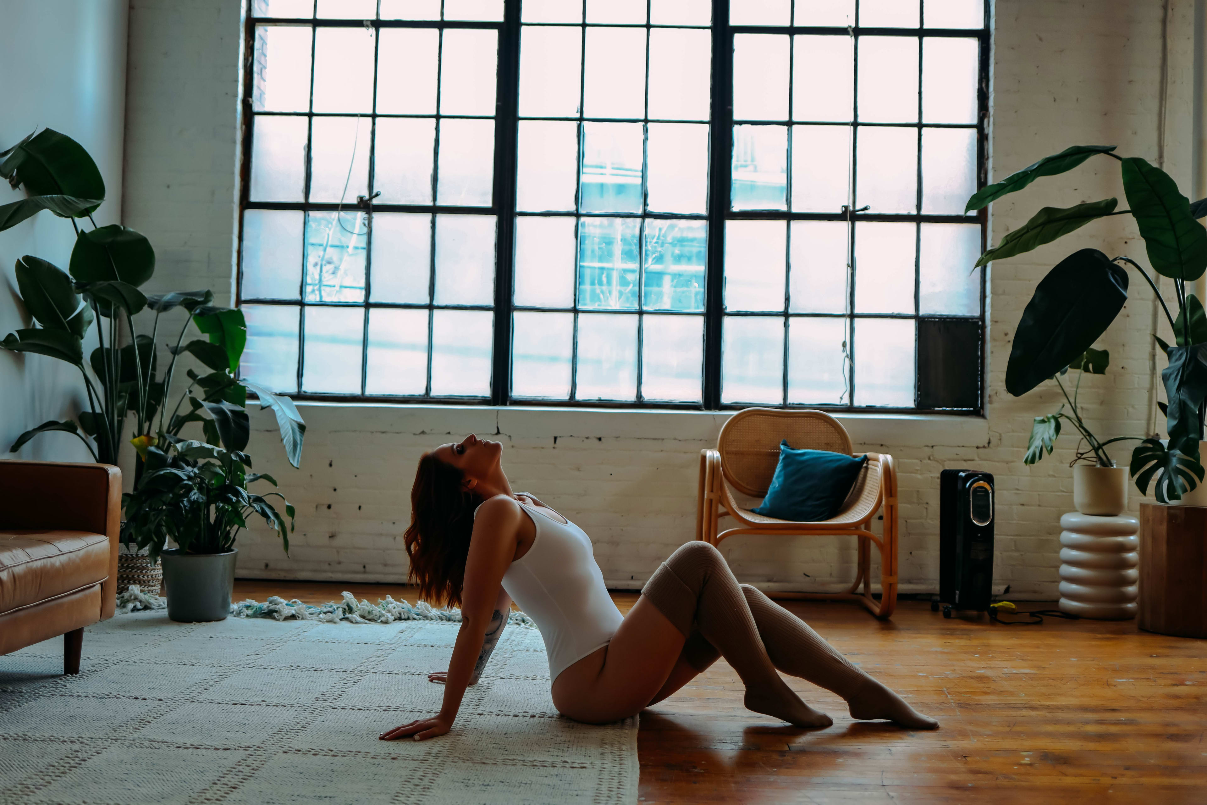 A woman is lying on the white floor in front of a window in a boho warehouse.
