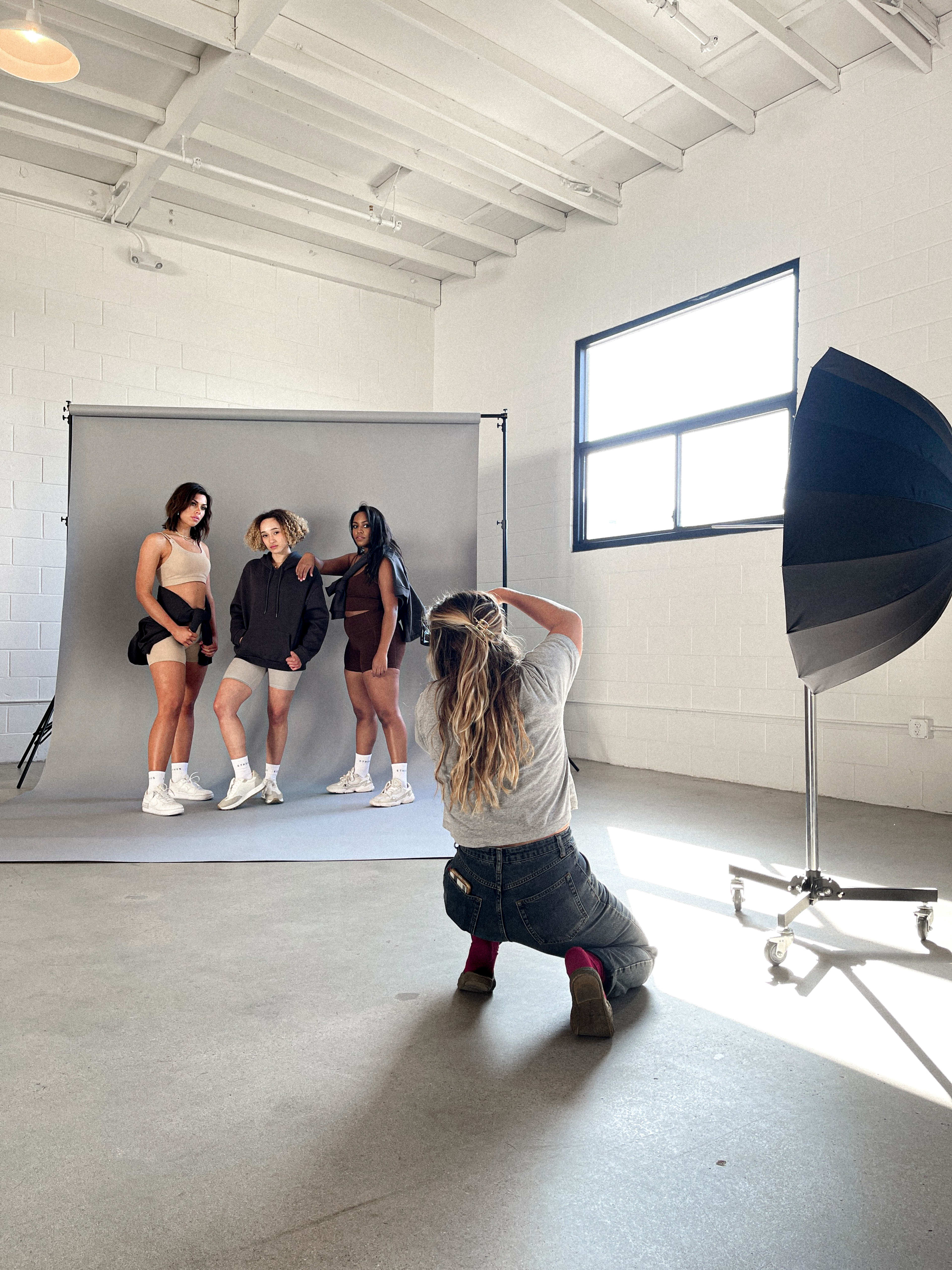 Ein weiß-graues Fotoshooting hinter den Kulissen mit einer Gruppe von Frauen, die für Fotos von Fitnessprodukten posieren.