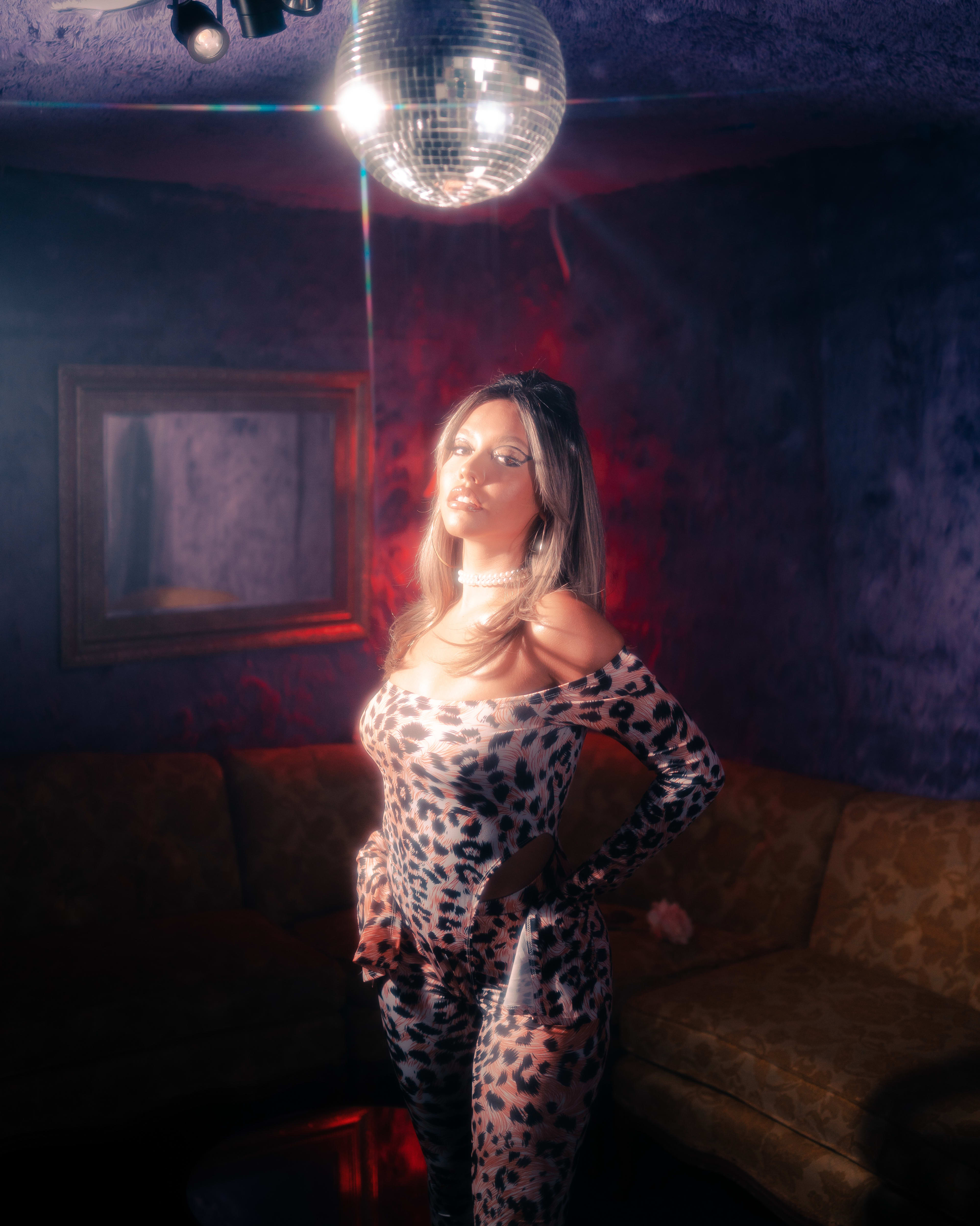 A retro photoshoot of a woman posing in a room with a disco ball hanging from the ceiling.
