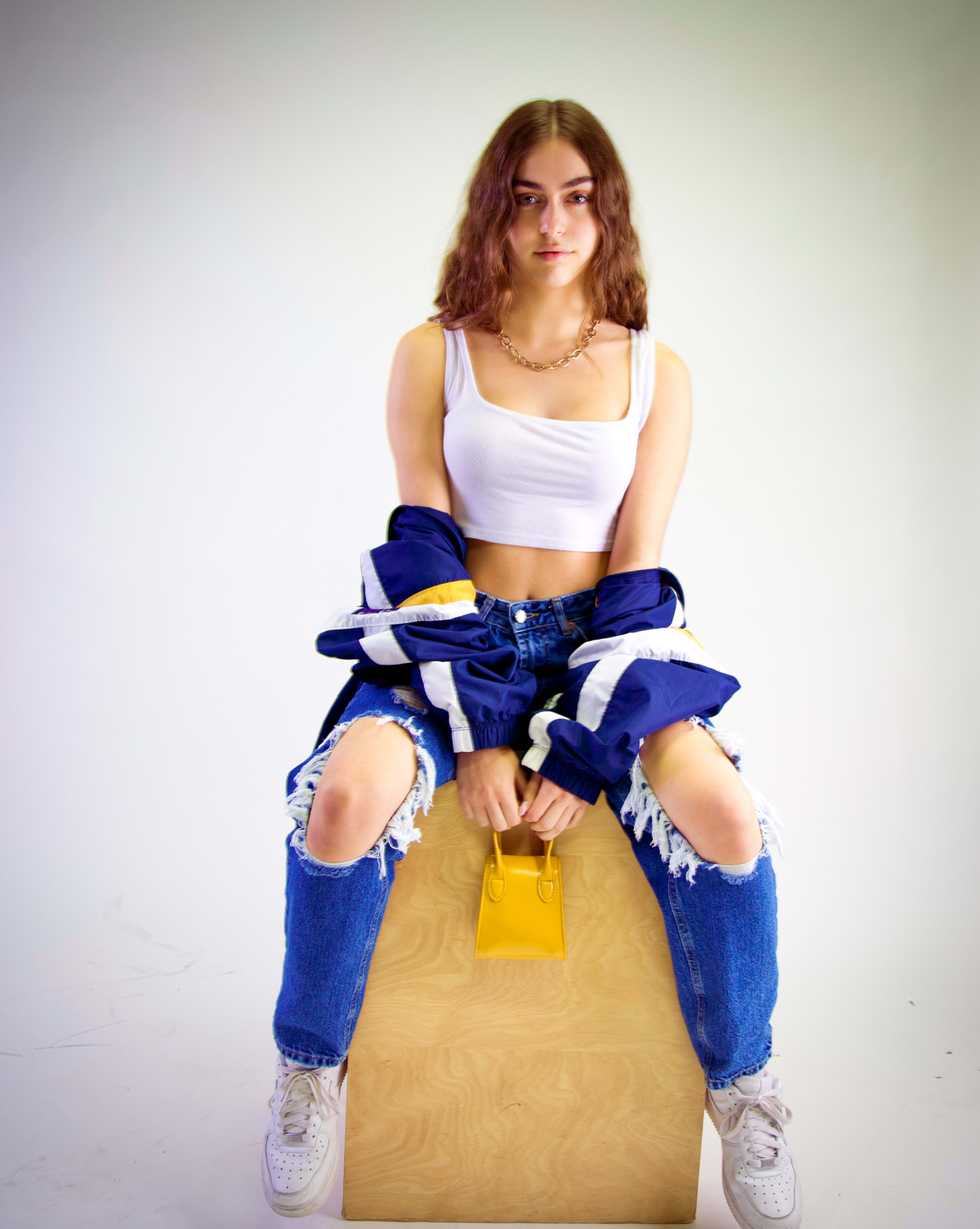 A woman with a yellow purse posing on top of a wooden box during a fashion photoshoot.