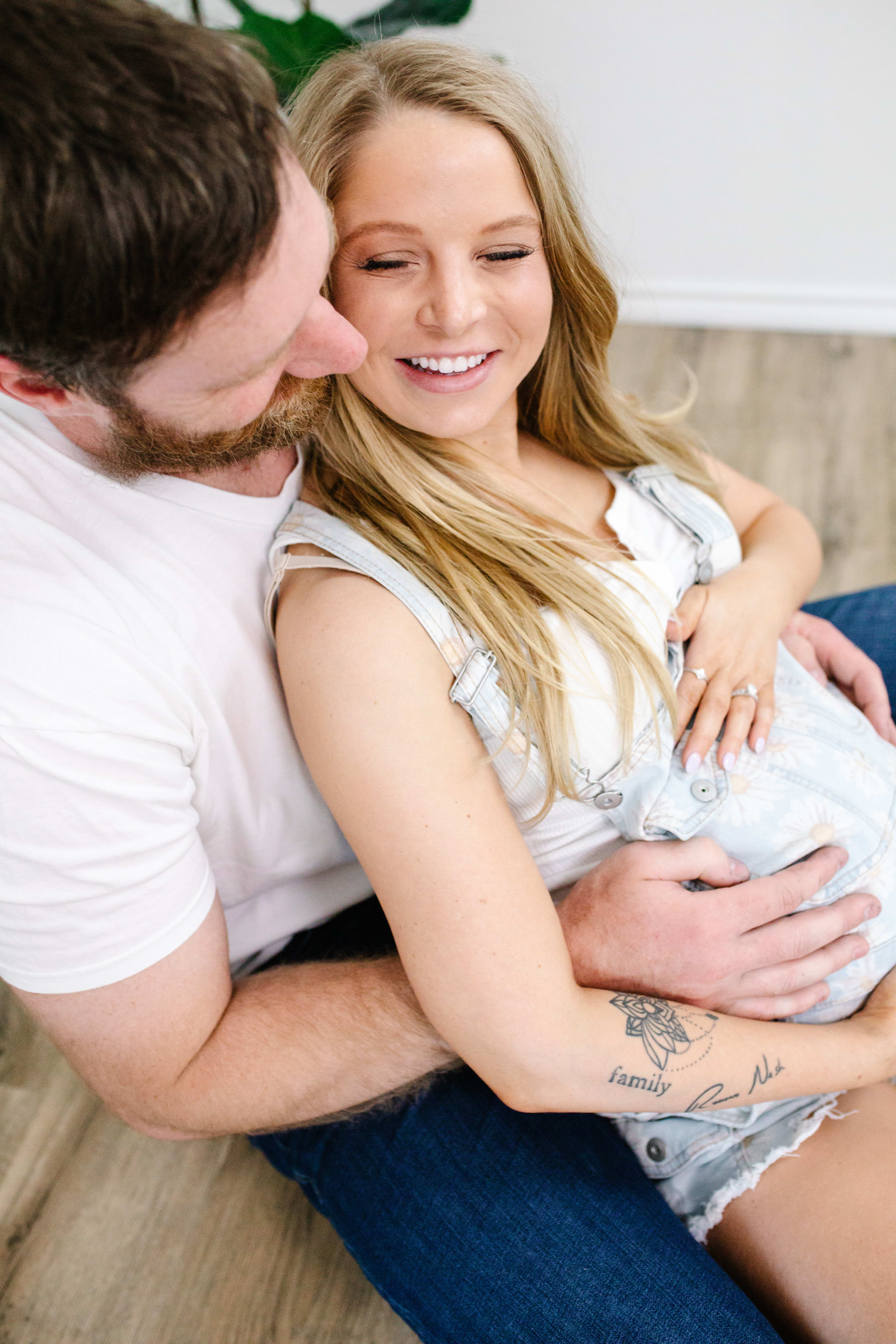 Una pareja durante una sesión de fotos de maternidad, sentada en el suelo.