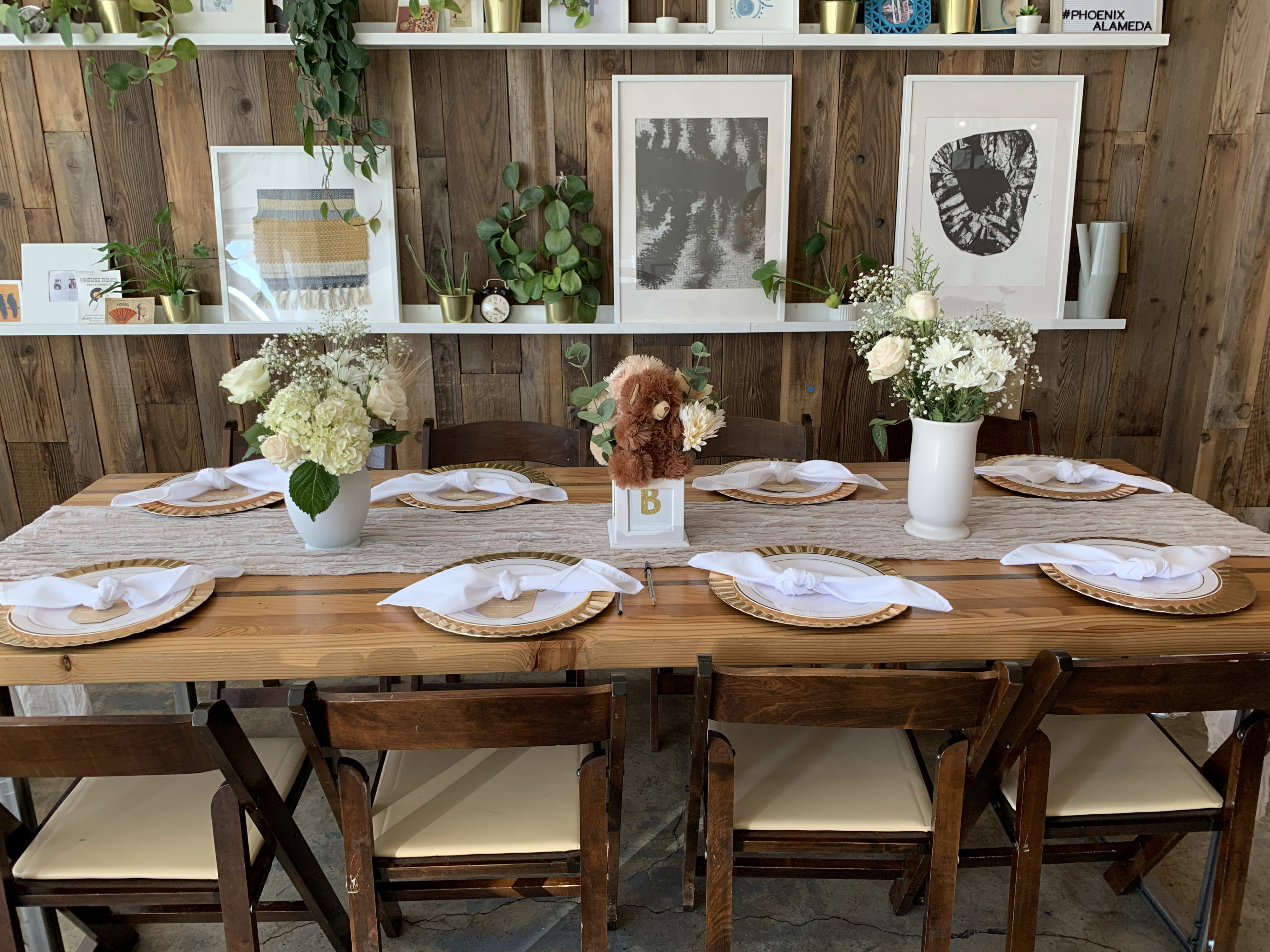 Una mesa rústica de madera adornada con jarrones de flores para un brunch de baby shower de género neutro.