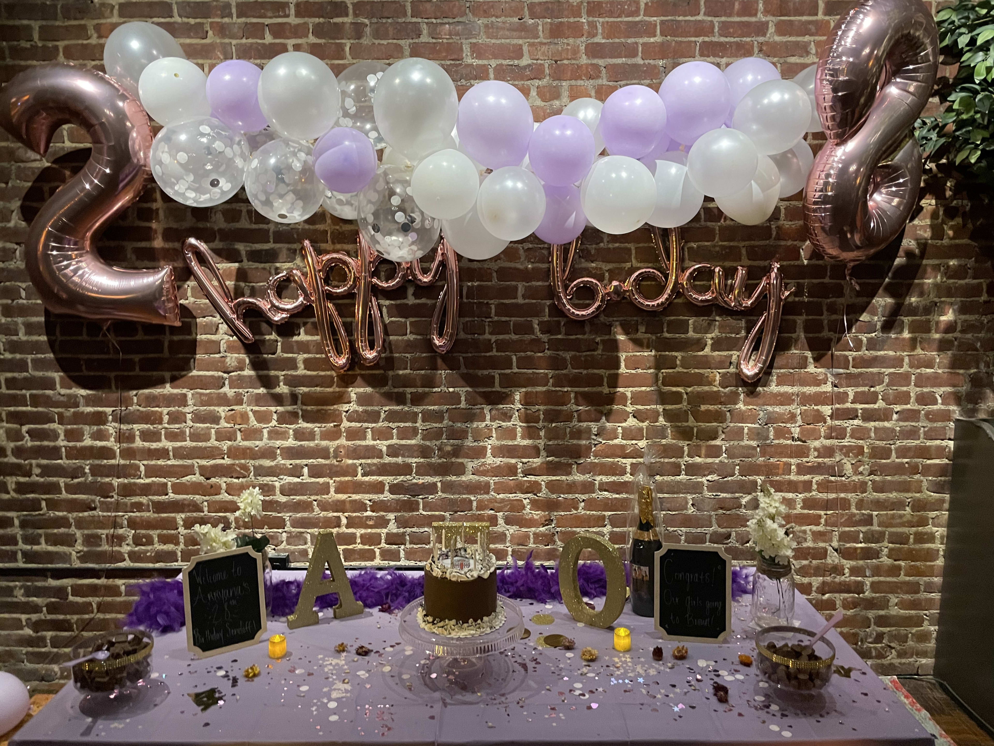 A birthday party table with a cake and purple and white balloons.