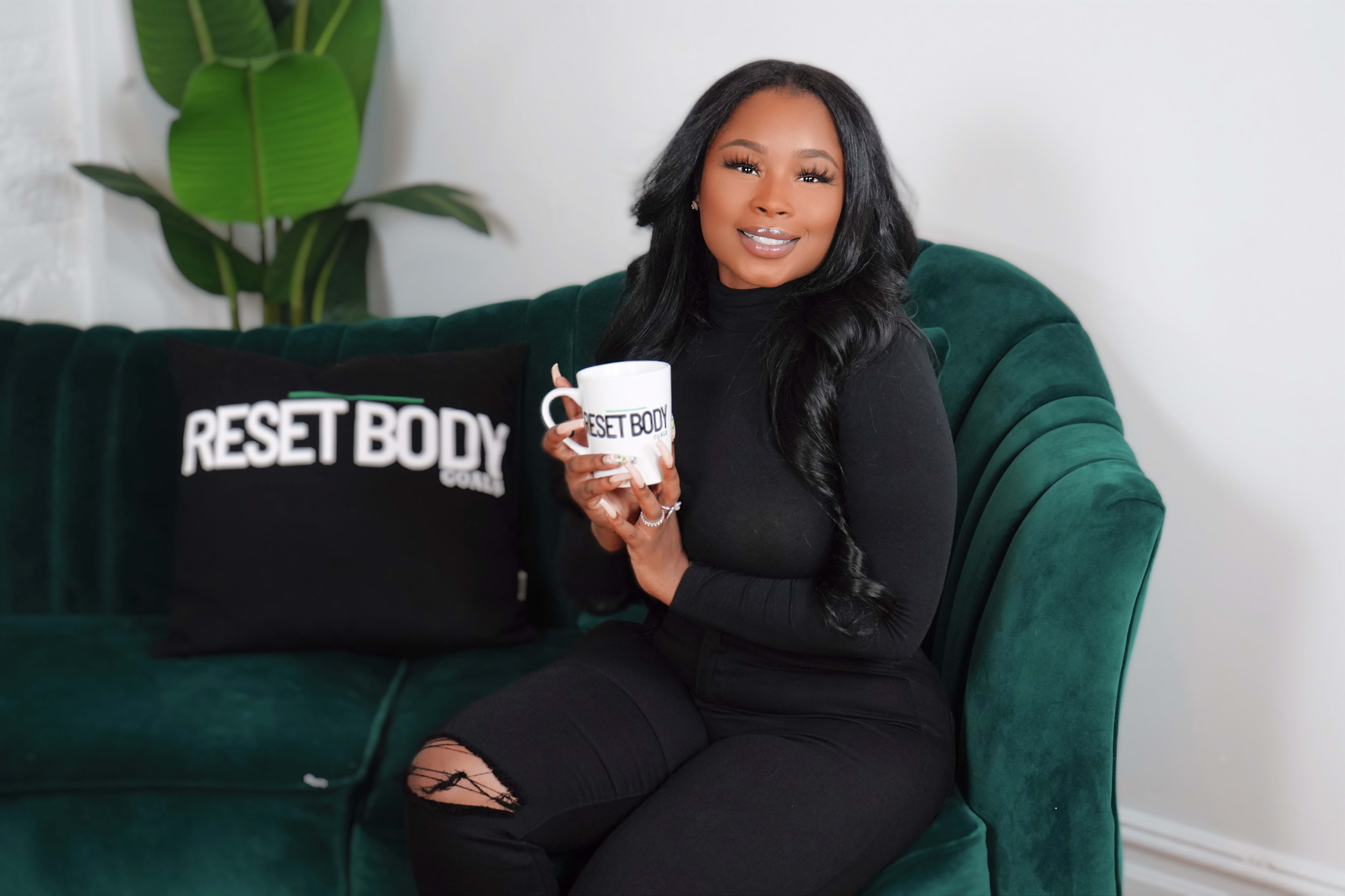 A woman sitting on a green couch holding a black coffee mug.