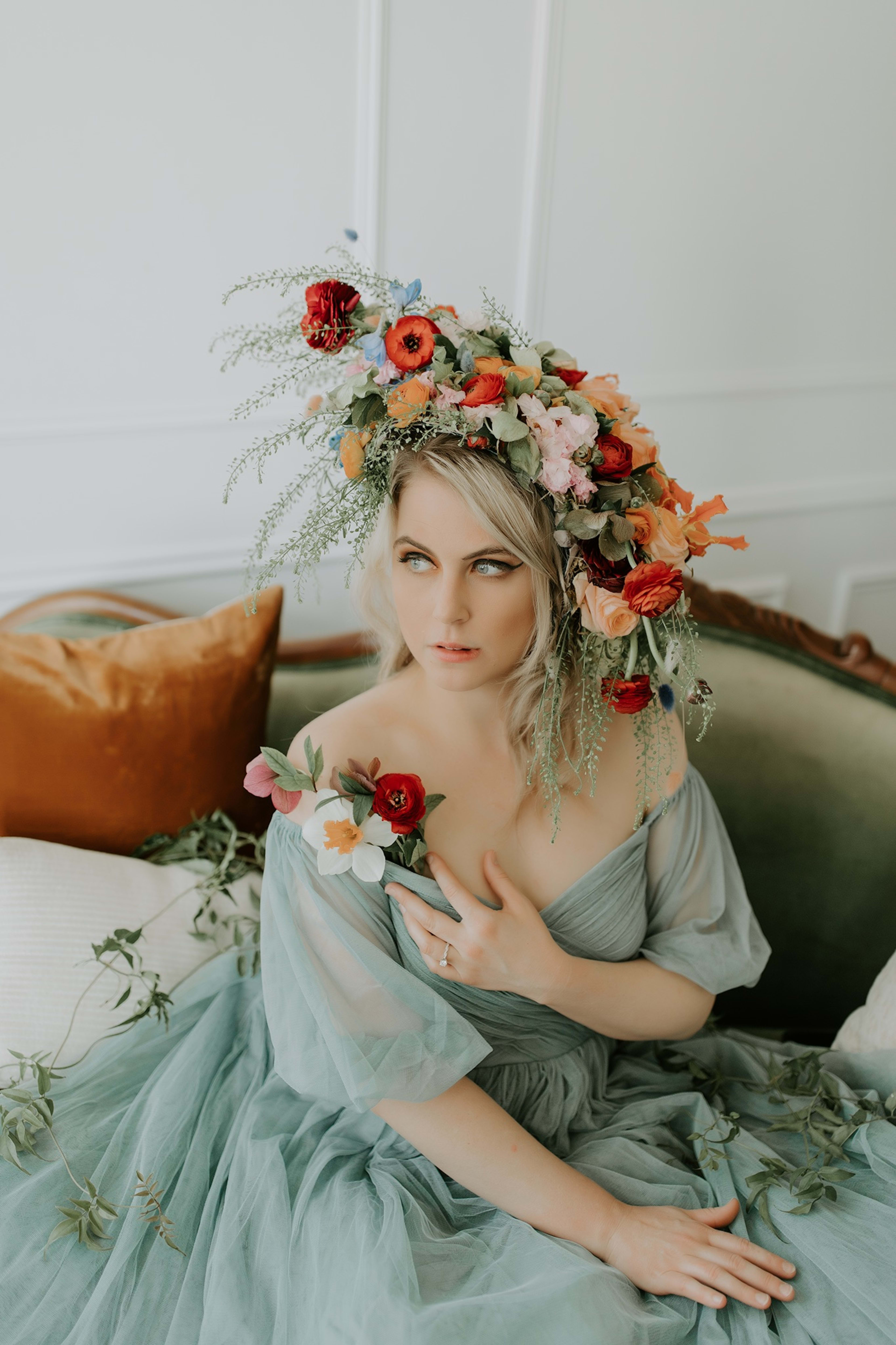 A Victorian-themed photoshoot featuring a woman wearing a flower crown sitting on a green and white couch.