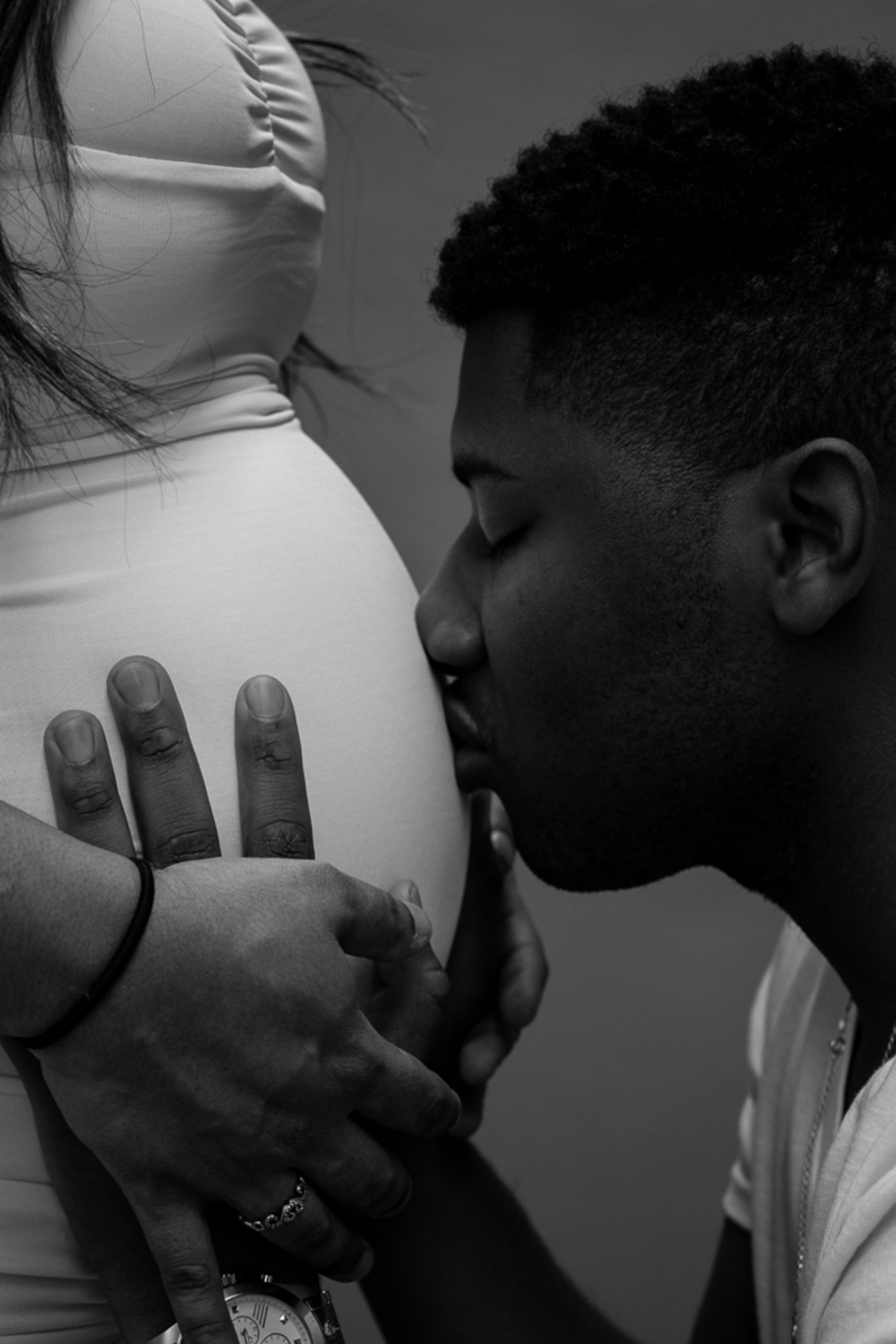 Un shooting photo en noir et blanc mettant en scène un homme embrassant une femme enceinte.