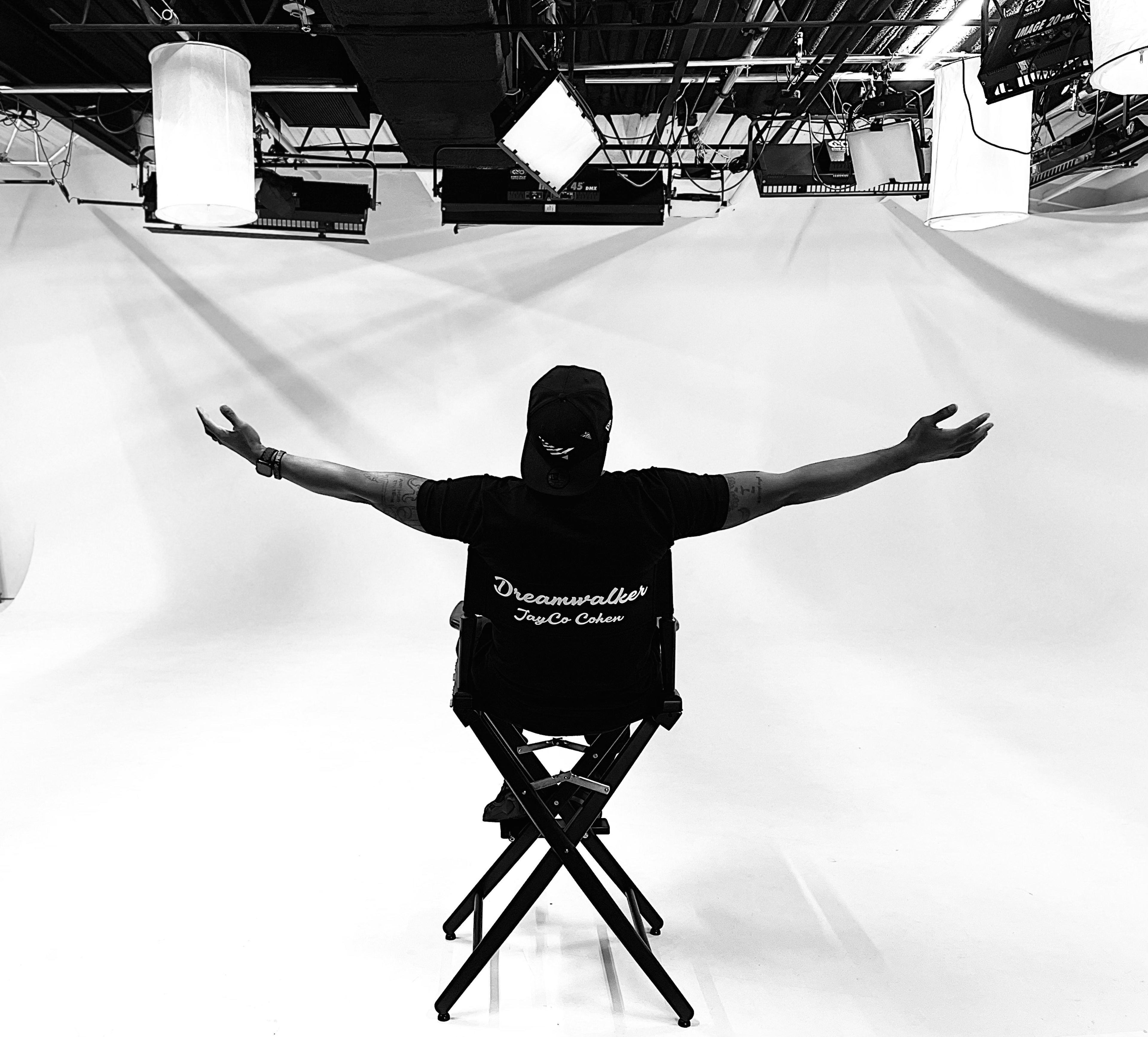 A man posing for a black and white photoshoot with his arms outstretched in a chair.